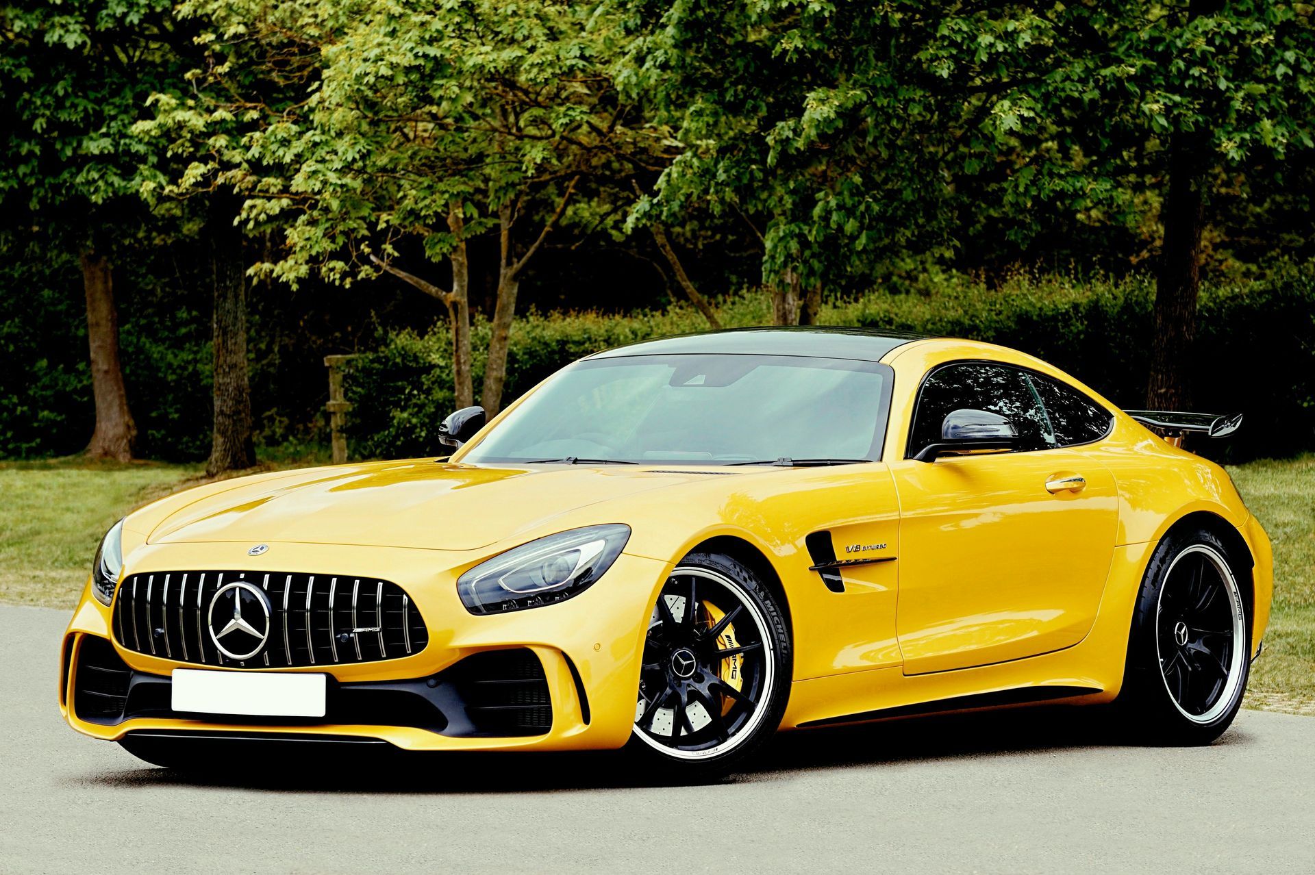 Yellow Mercedes-AMG GT sports car parked on a road with trees in the background.