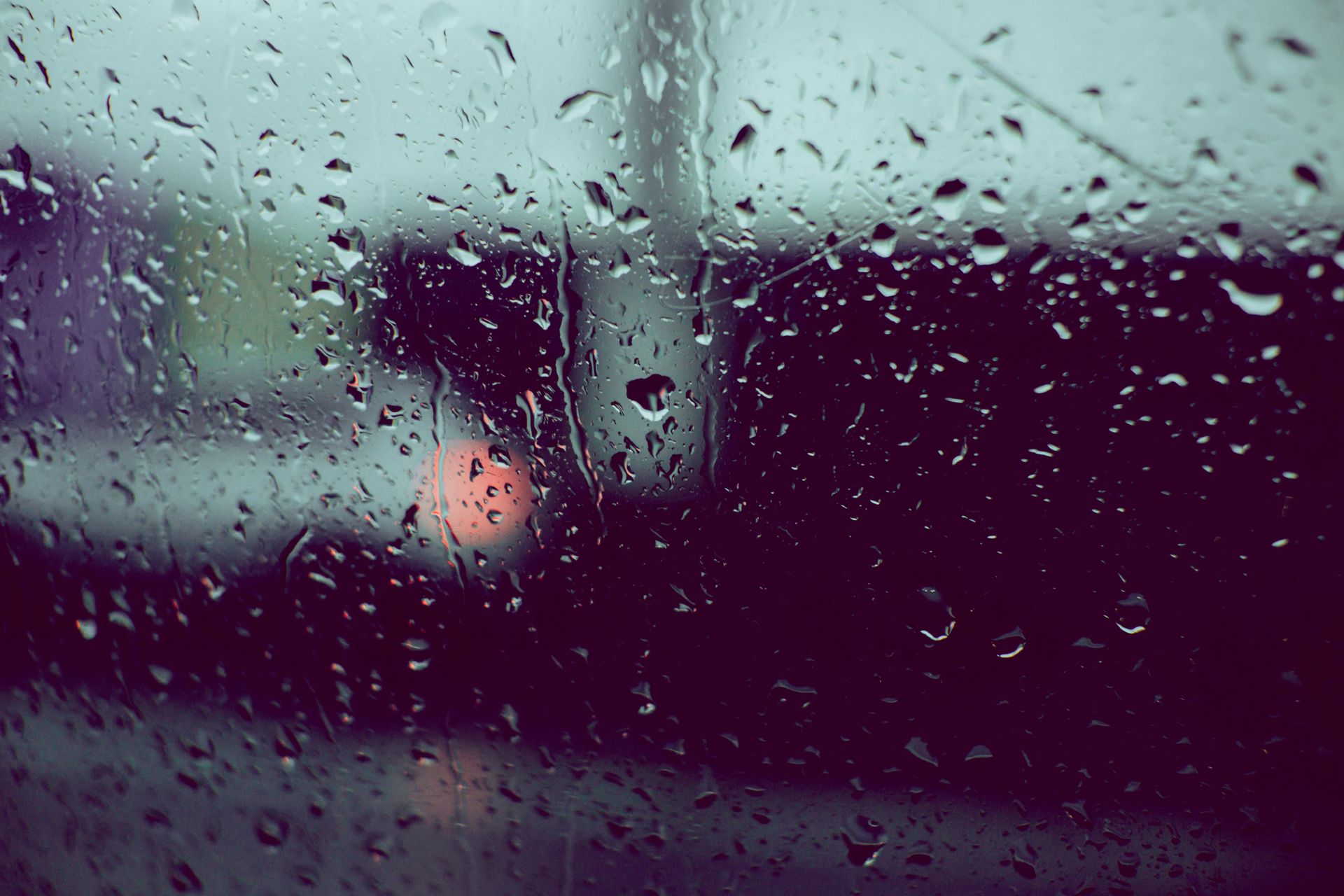 Raindrops on a window obscure blurry, dark city view with a red/orange light.