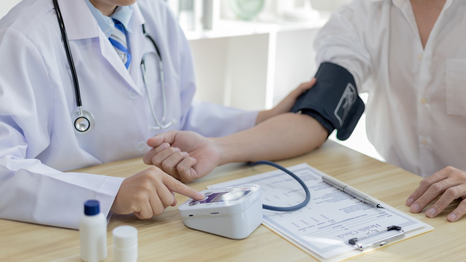 Doctor taking a patient's blood pressure with an electronic monitor in an office.