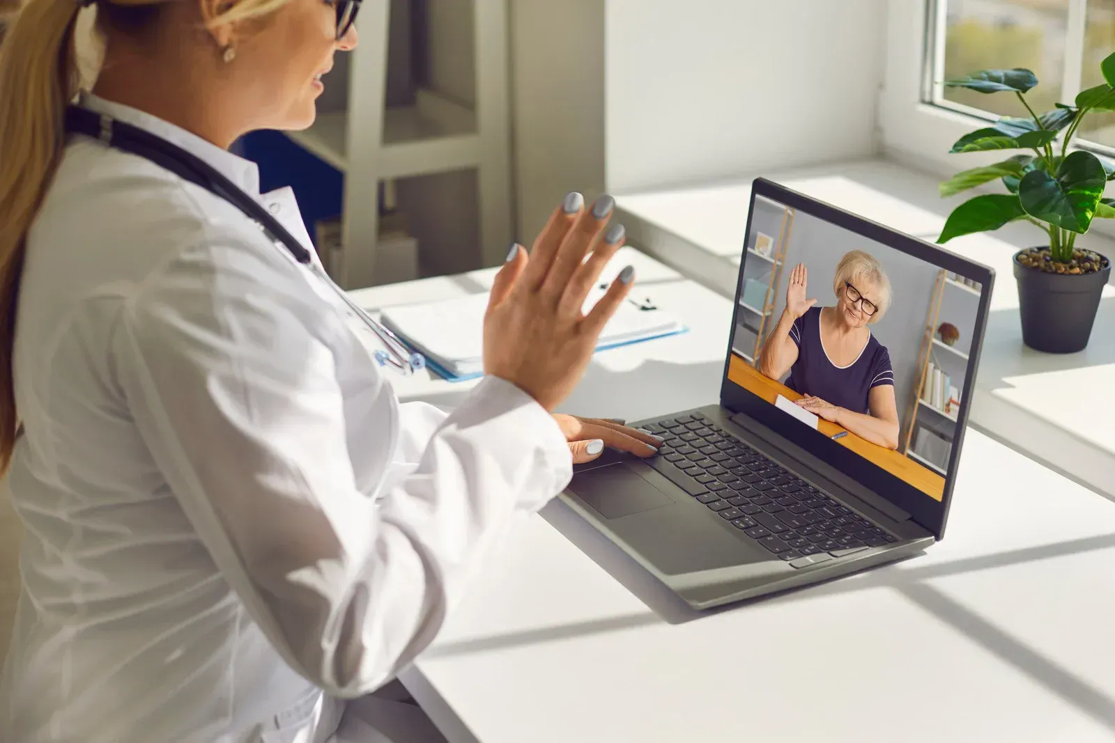 Doctor in white coat on video call with patient; patient waves.