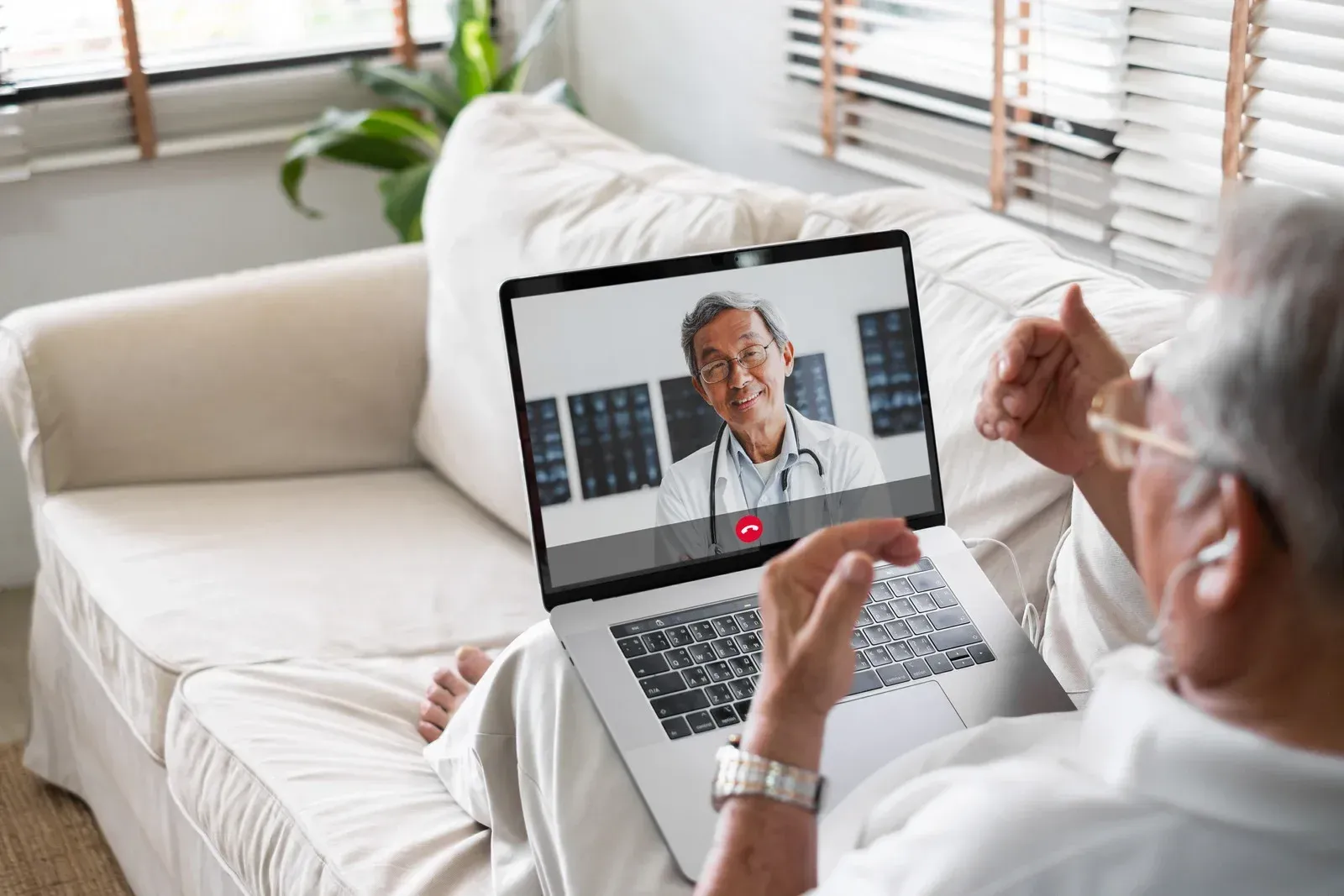 An older person having a telehealth appointment on a laptop, lying on a couch.
