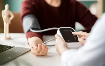 Doctor taking patient's blood pressure with an electronic monitor in an office setting.