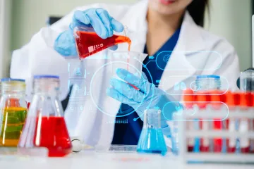 Scientist pours red liquid into a beaker, surrounded by colorful lab equipment.