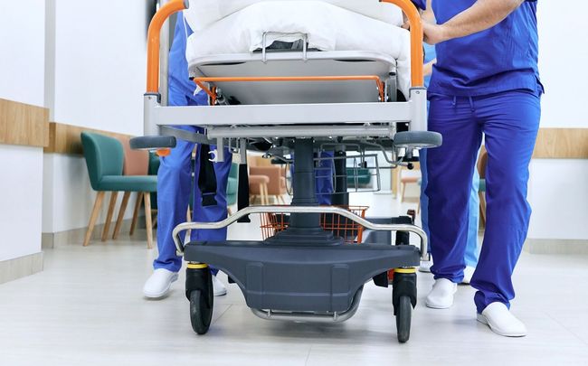 Medical personnel pushing a patient on a stretcher through a hospital hallway.