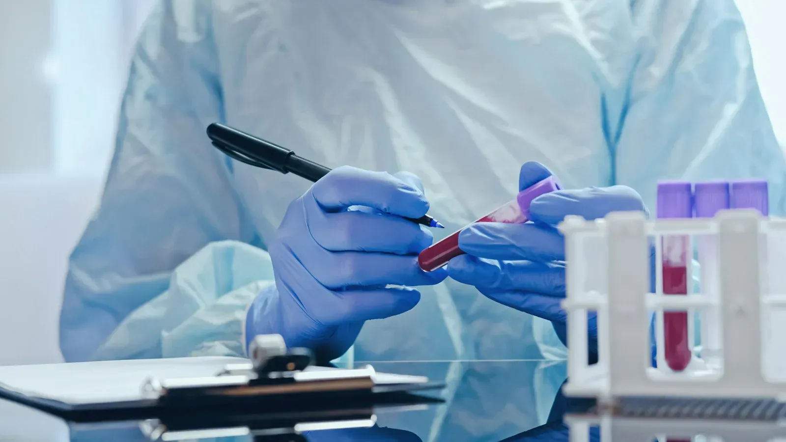 Person in blue medical gloves, writing on a blood sample tube.