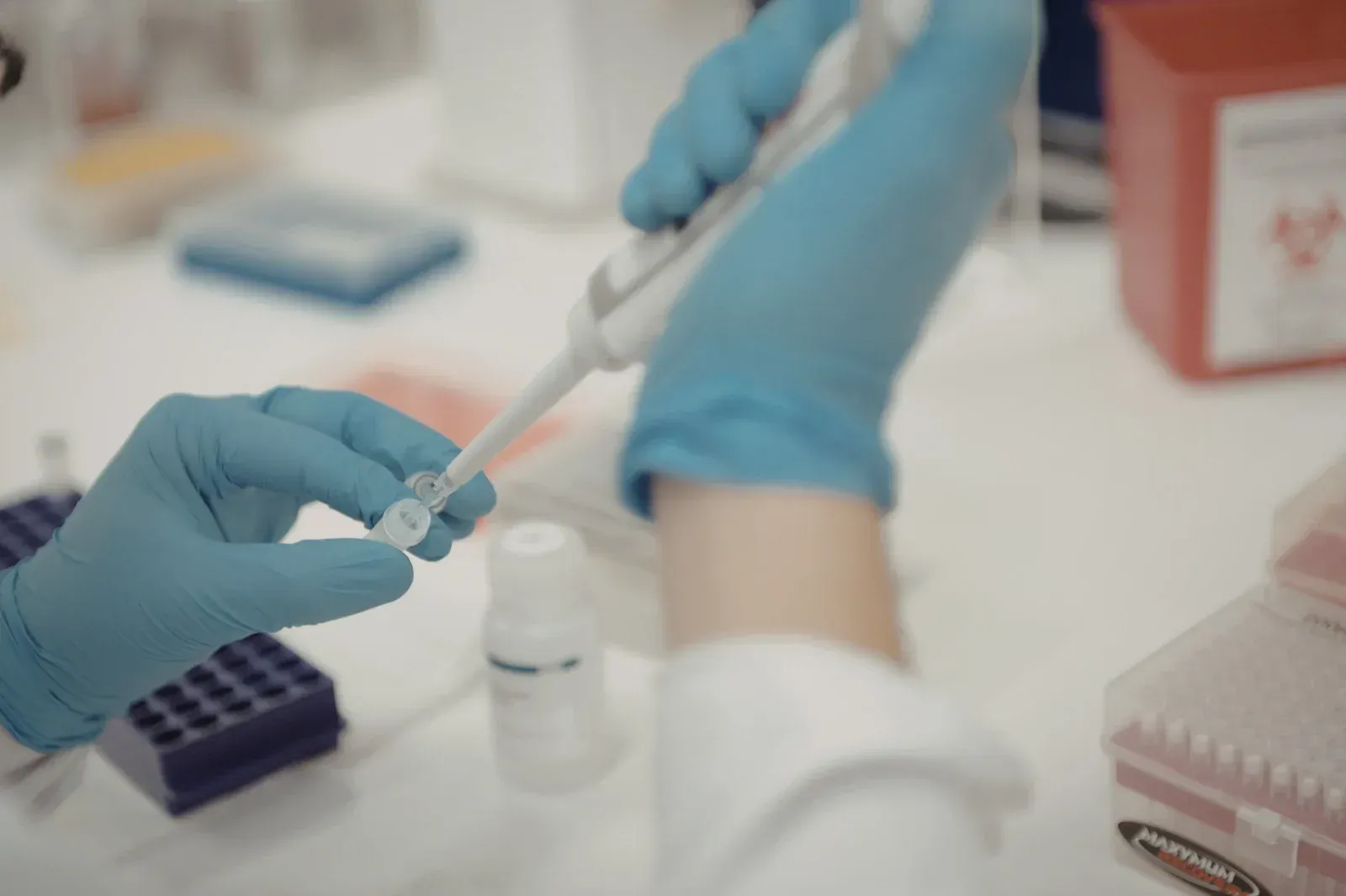 Person in blue gloves using a pipette to dispense liquid into a vial in a lab setting.