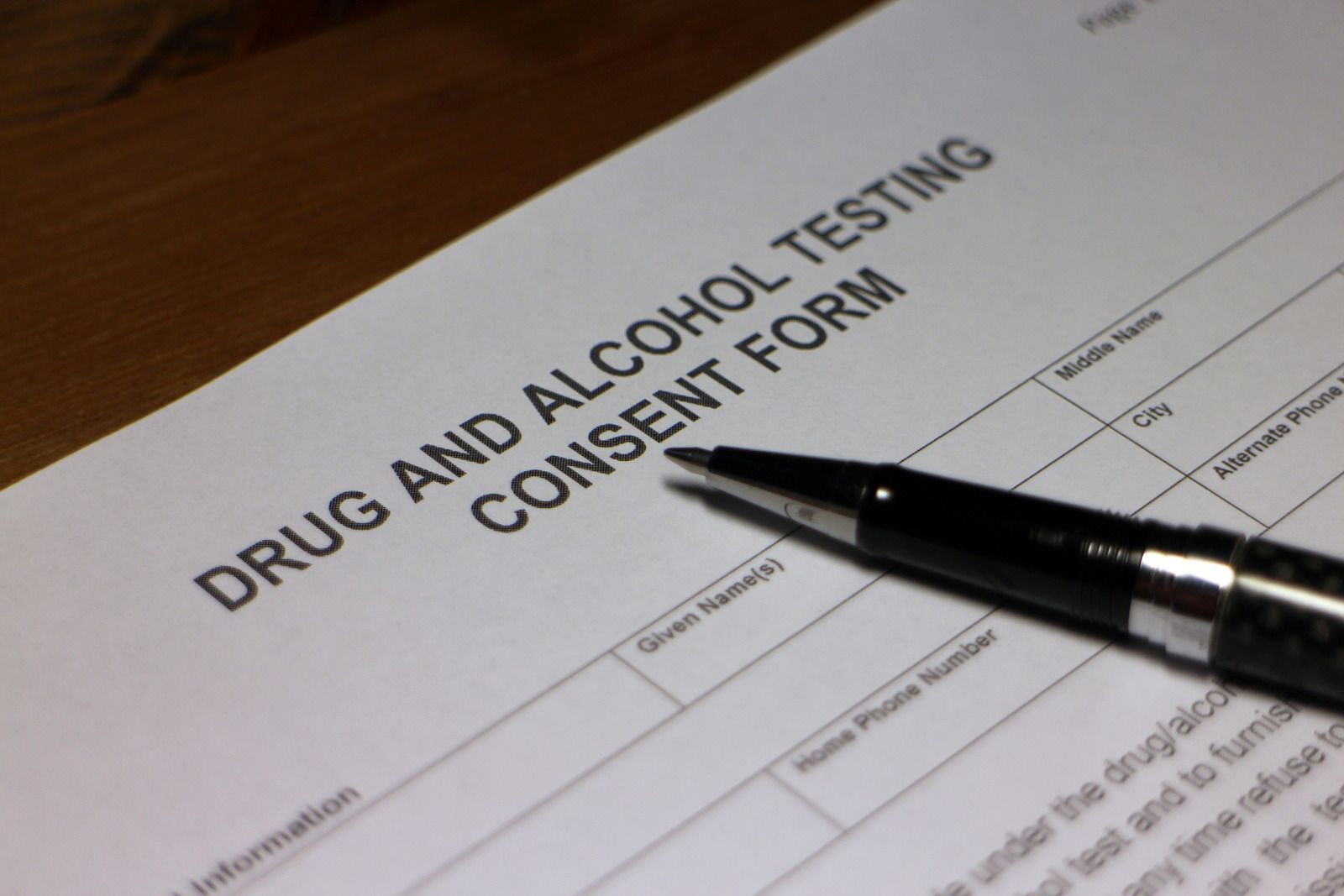 Drug and alcohol testing consent form with a pen on top, sitting on a wooden surface.