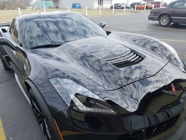 Black Chevrolet Corvette sports car parked in a lot, reflecting the sky.