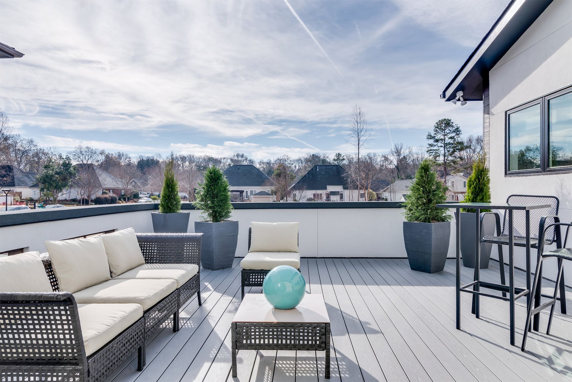 a rooftop deck with a couch , chairs , table and potted plants .