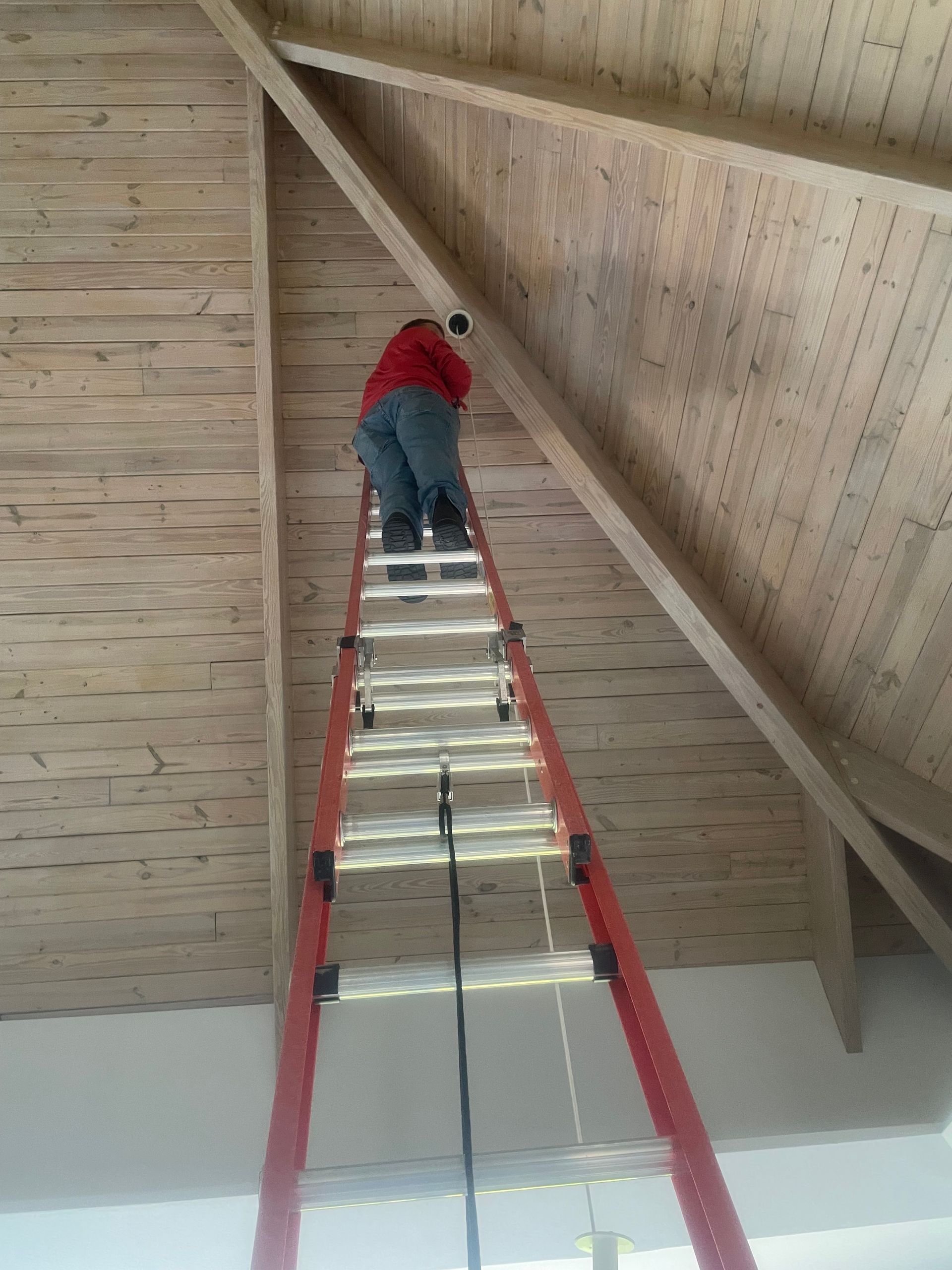 Person in red shirt climbs a ladder to a loft ceiling with exposed wooden beams.