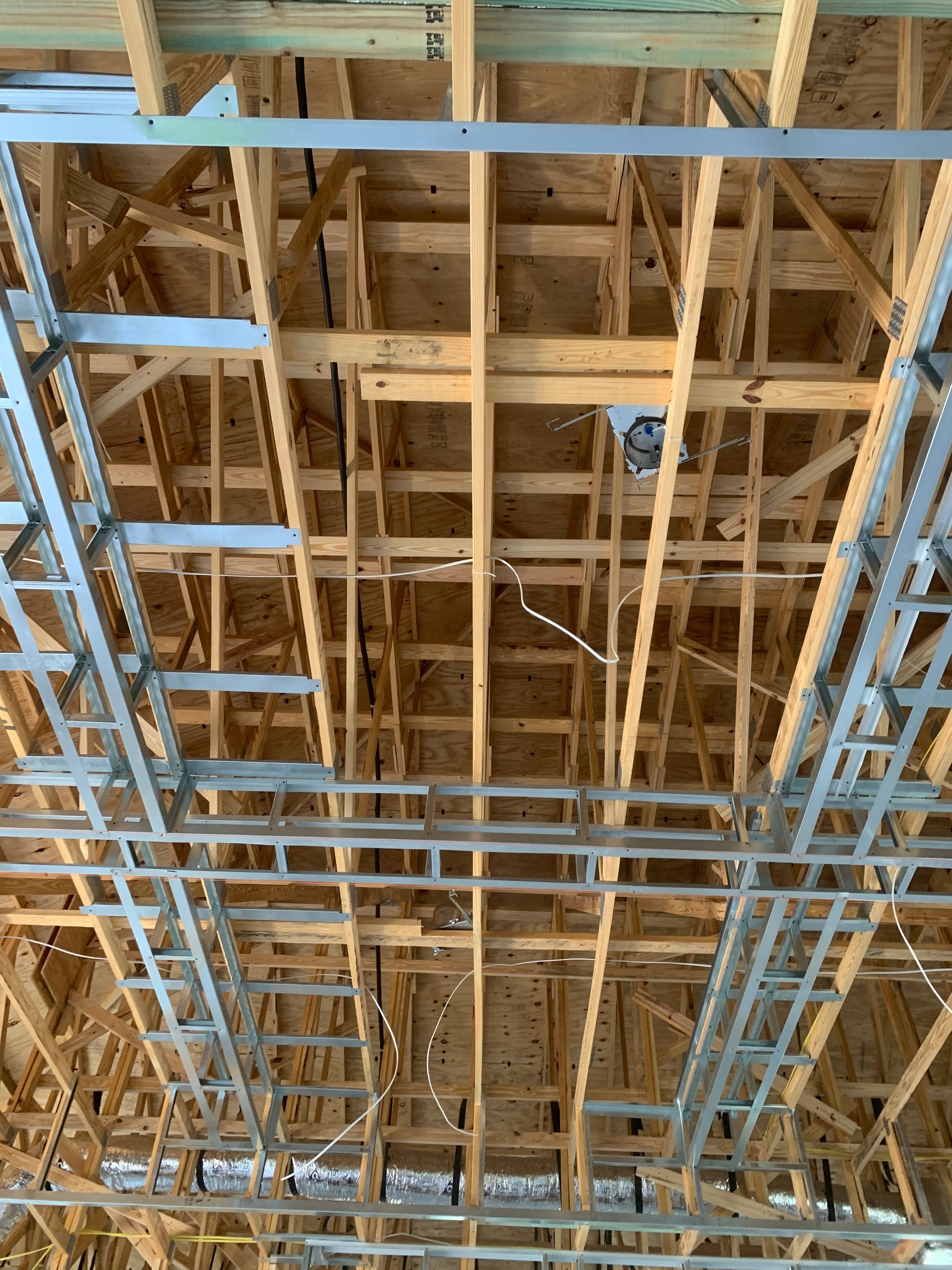 Exposed wooden ceiling framing with blue metal scaffolding and ducts in an unfinished building interior