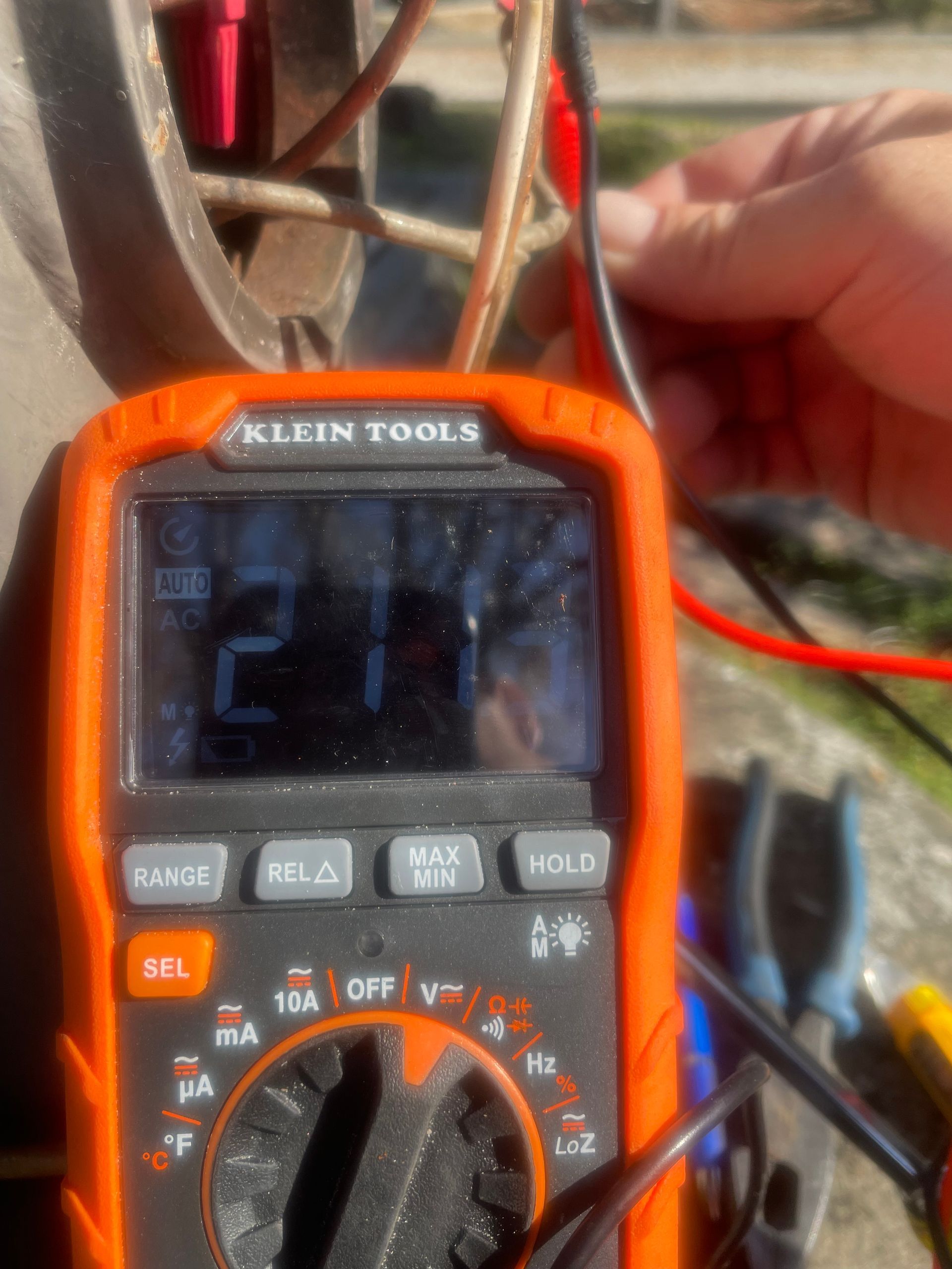 Orange Klein Tools multimeter showing 2.1, held near red and black test leads.