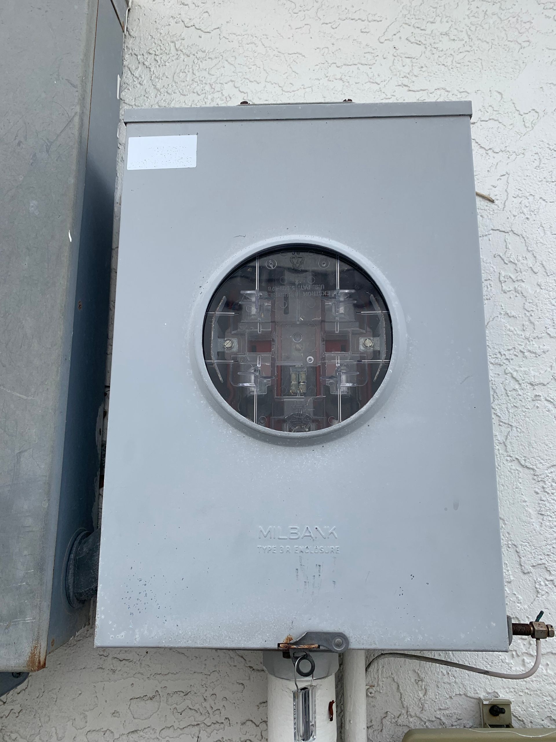 Gray electrical meter box mounted on a wall with a round glass meter window.