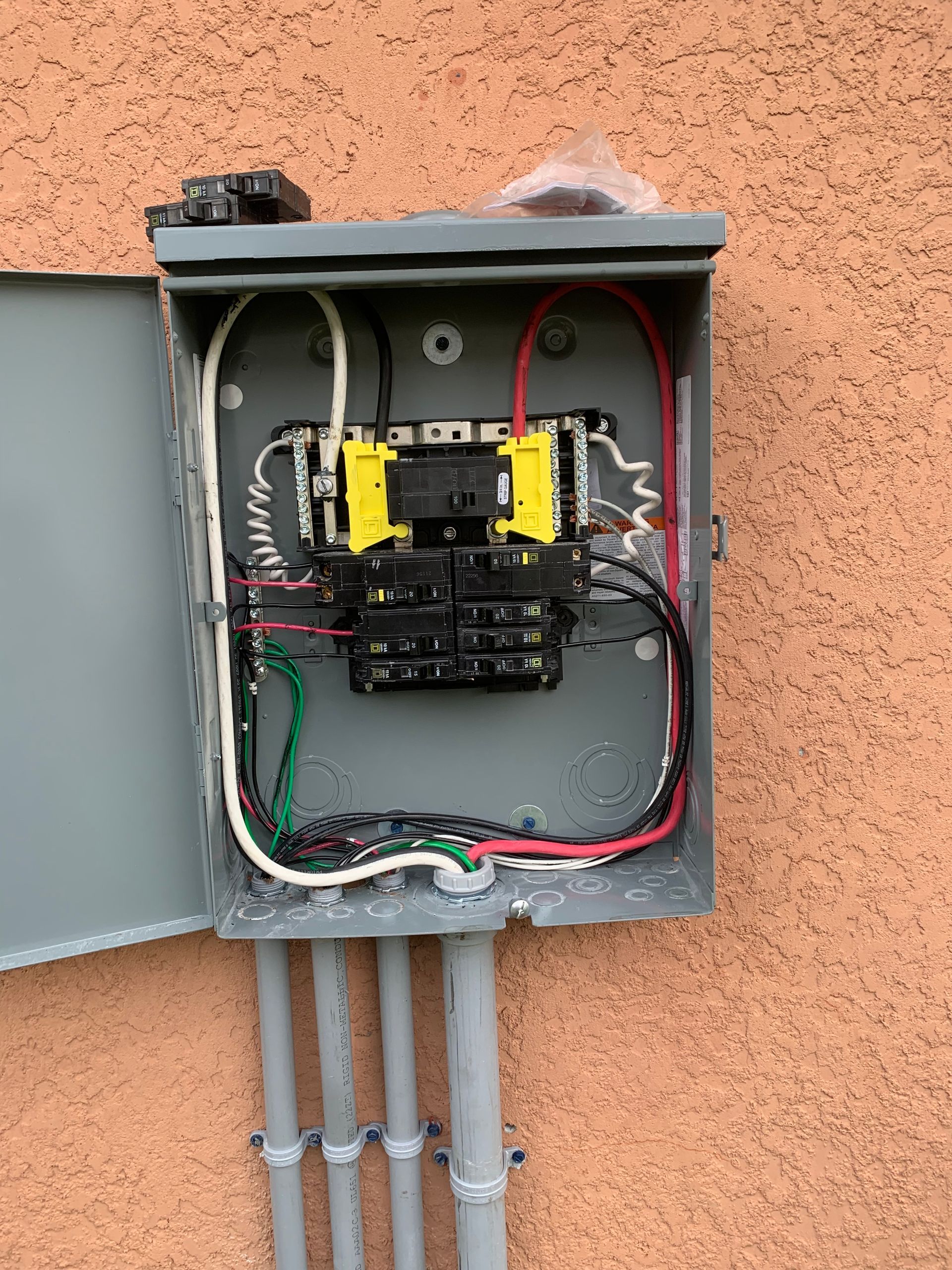 Open electrical breaker panel with exposed wiring in a gray wall box outdoors