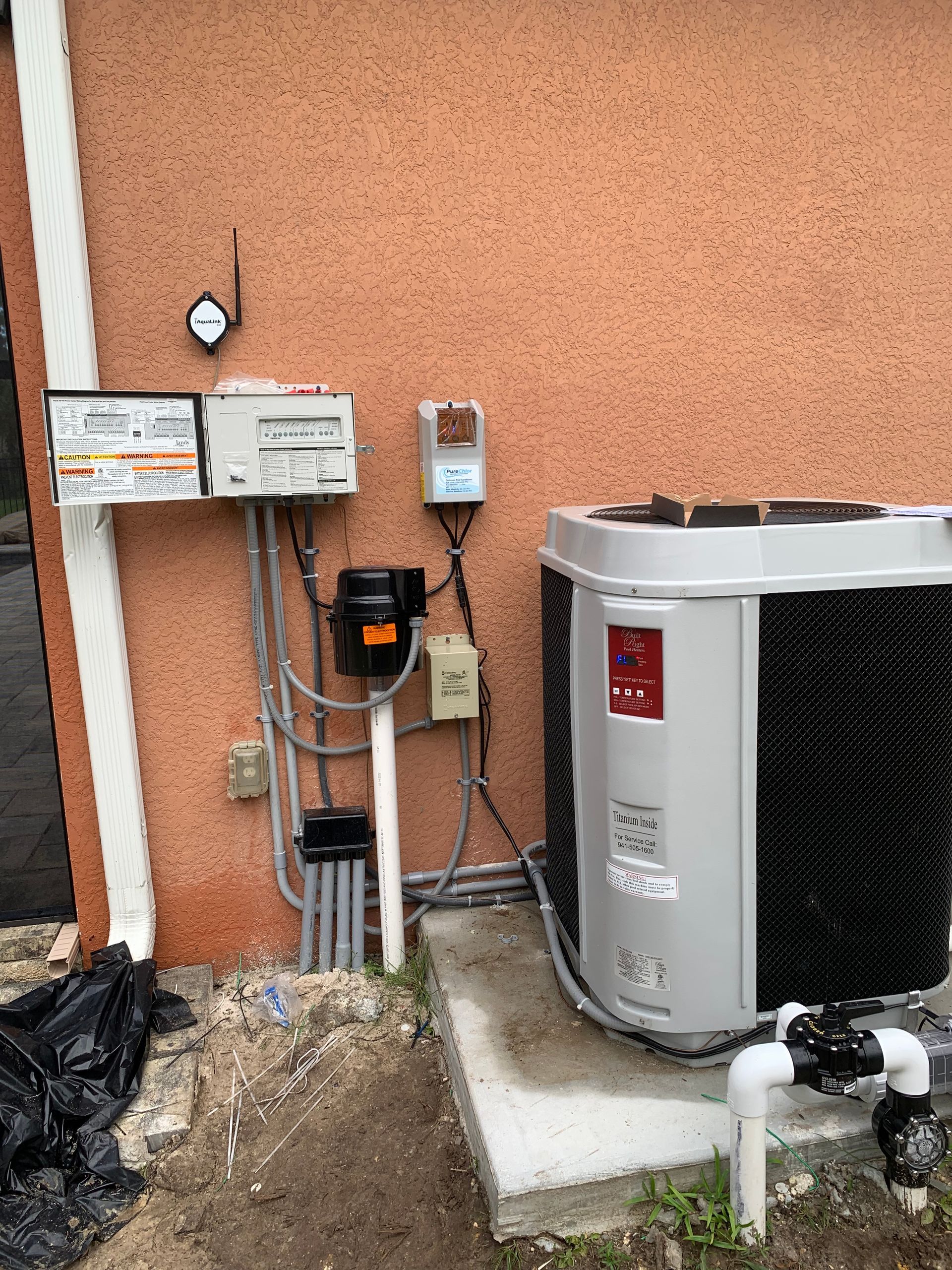 Outdoor utility meters, electrical boxes, and an air conditioner unit beside a stucco wall.