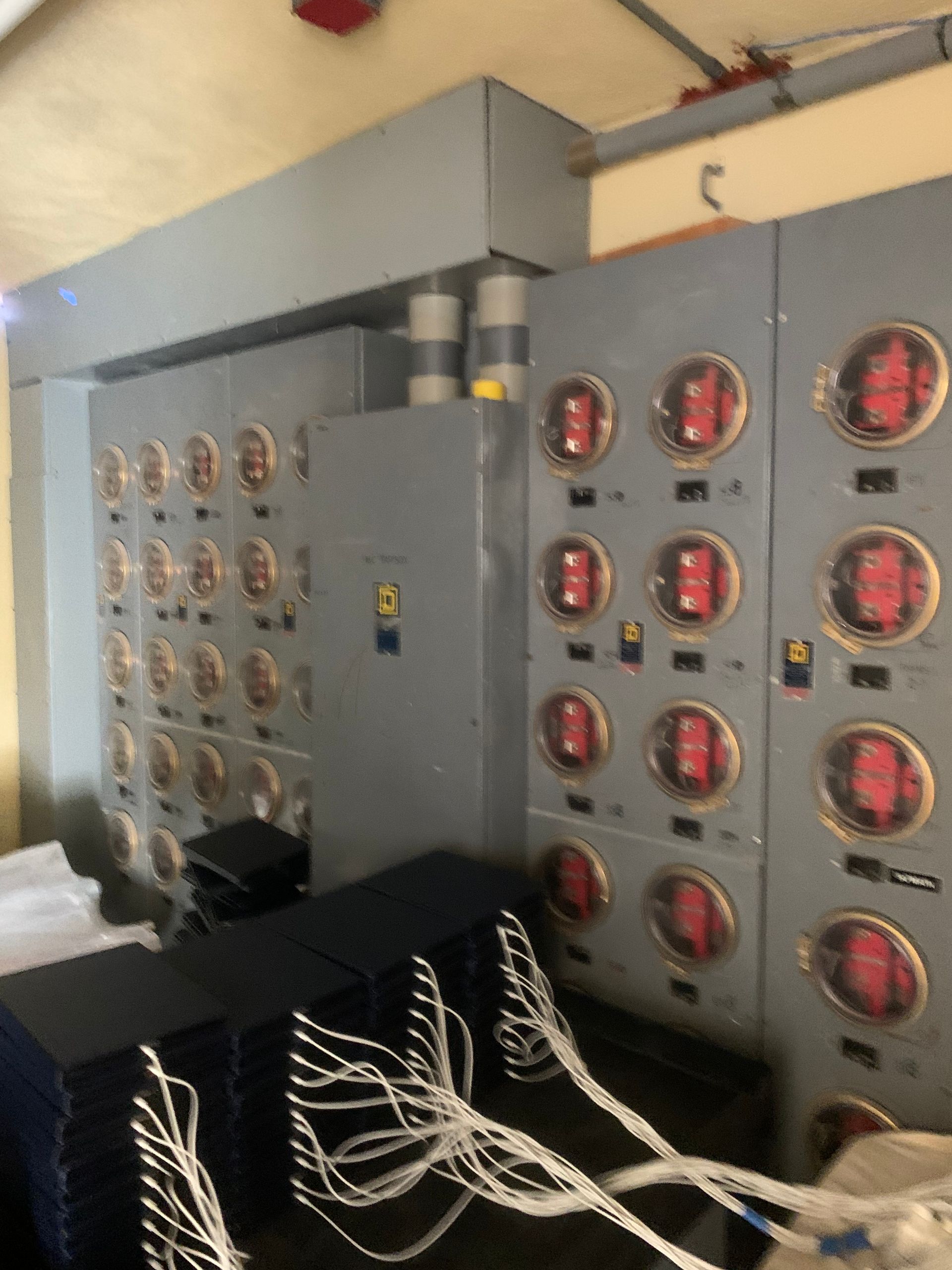 Industrial electrical control panels with red gauges and tangled white cables in a utility room