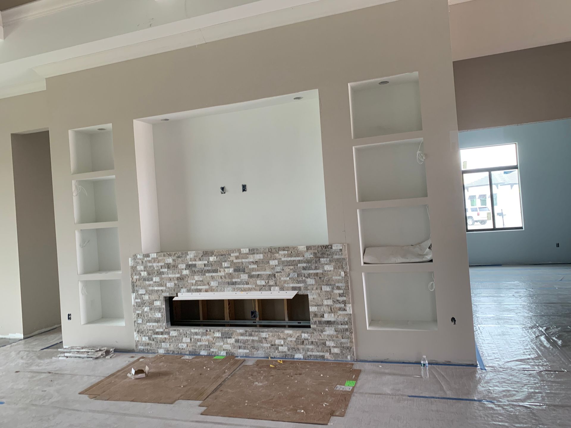 Renovated living room with built-in fireplace, white shelving, and partially covered floors