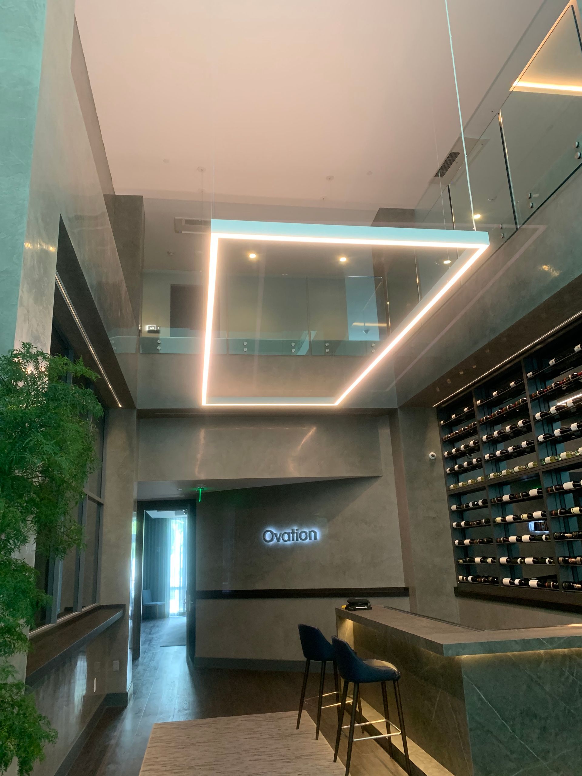 Modern wine bar interior with geometric ceiling lights, a wall of wine bottles, and seating area