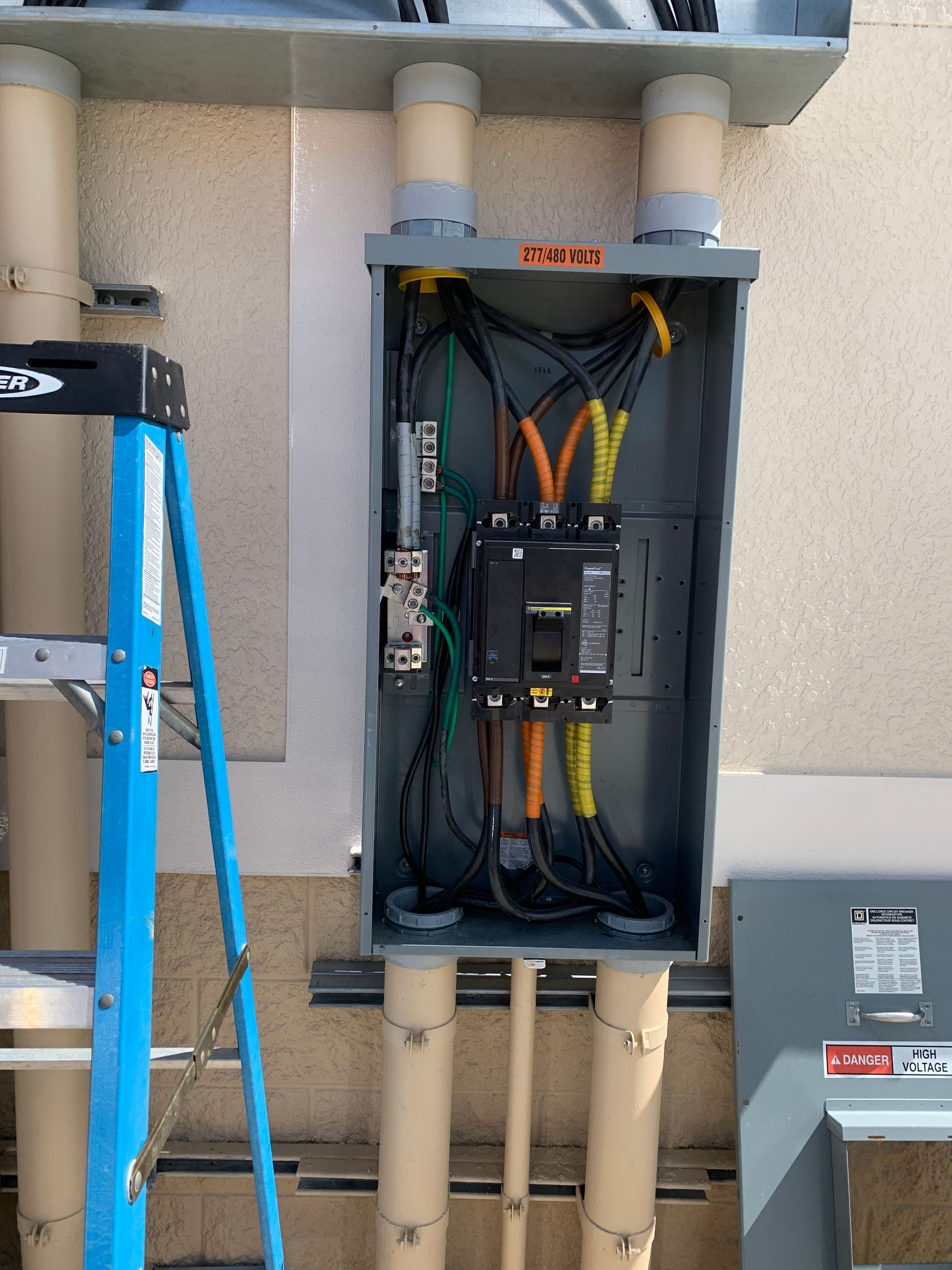 Open electrical service panel with wiring and breakers mounted on an exterior wall.