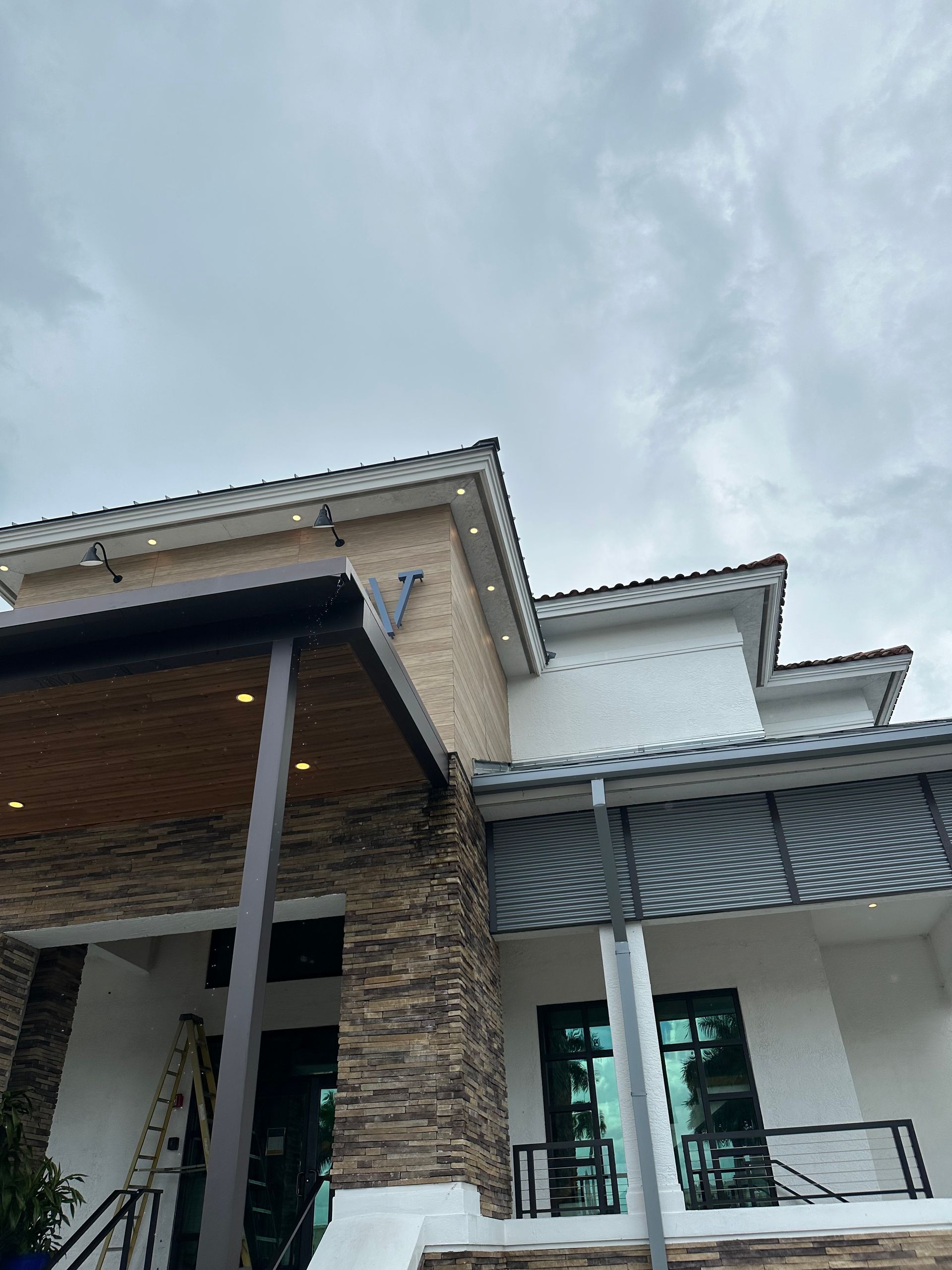 Low-angle view of a house exterior with stone columns, white trim, and a cloudy sky