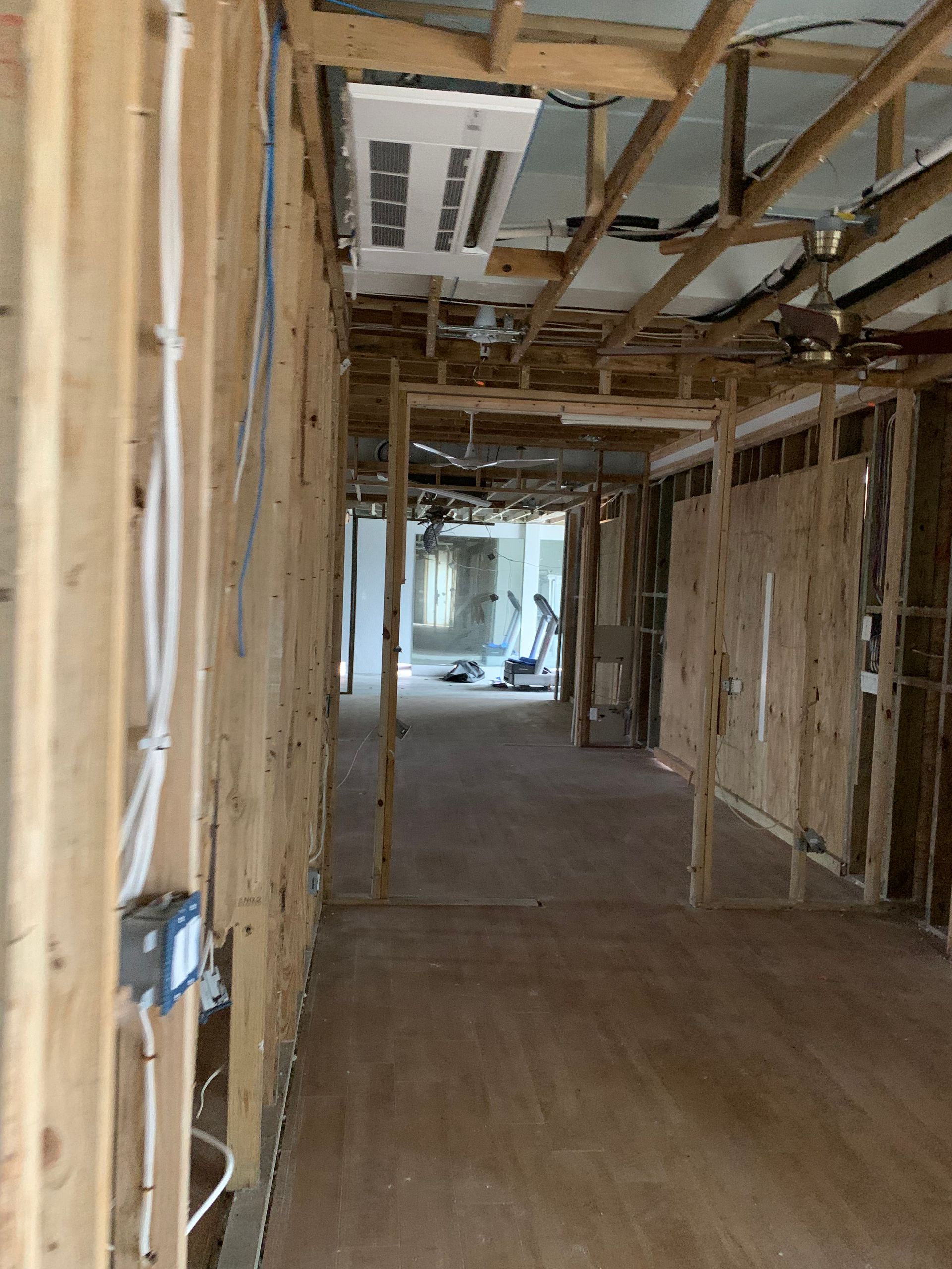 Damaged hallway interior with exposed studs, ceiling beams, and debris during renovation