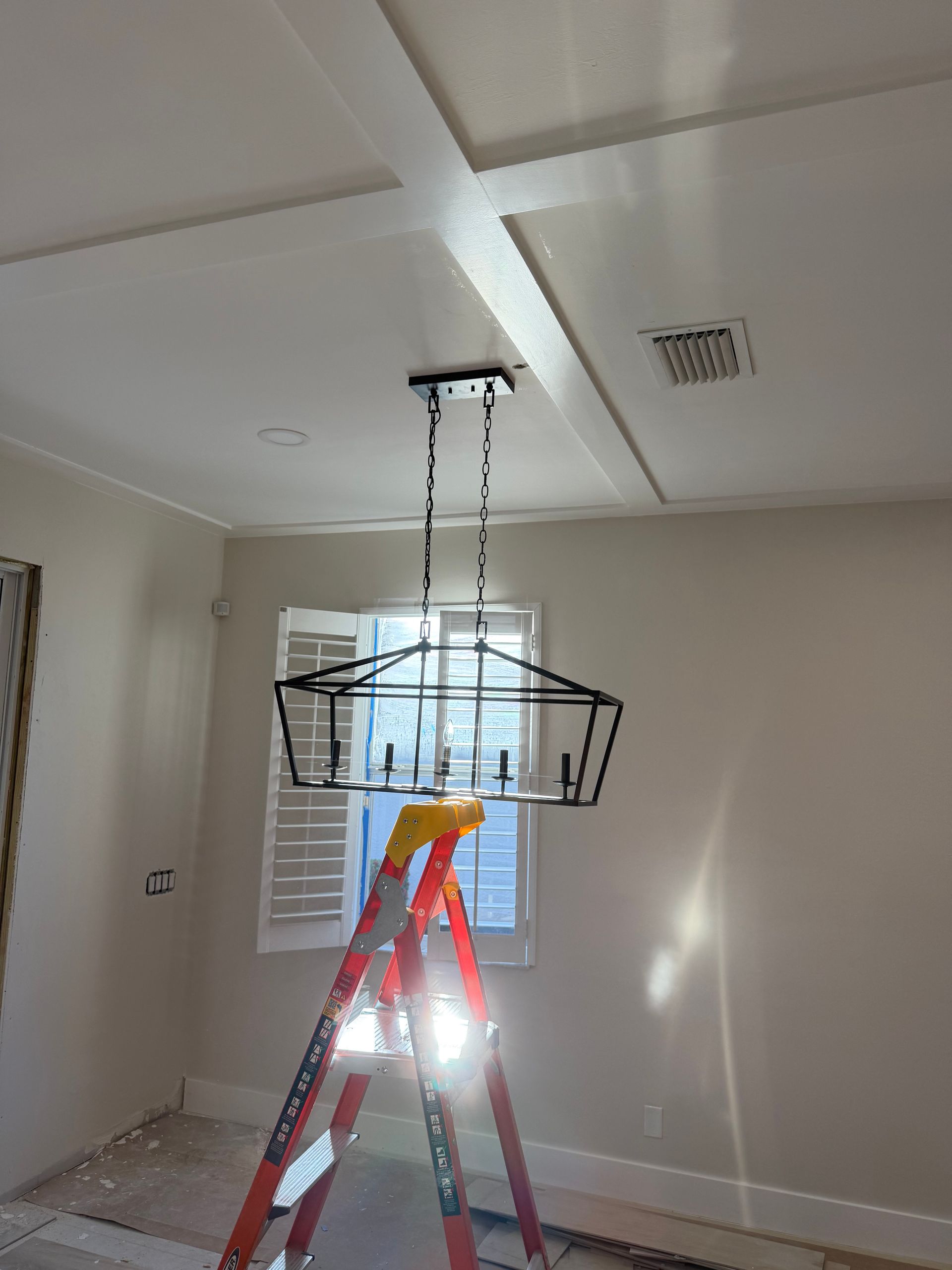 Red ladder in a room with a hanging wire basket under a ceiling fixture, near a window and beige walls