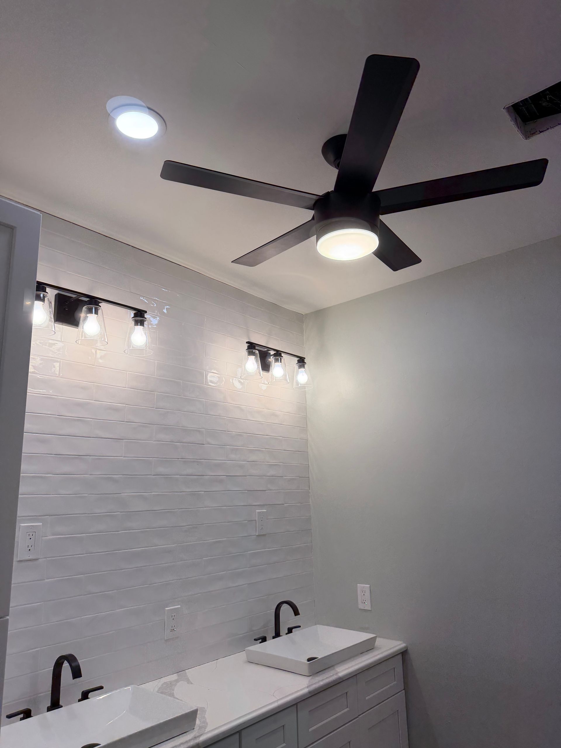 Modern bathroom with white tile wall, double vanity, and black ceiling fan.