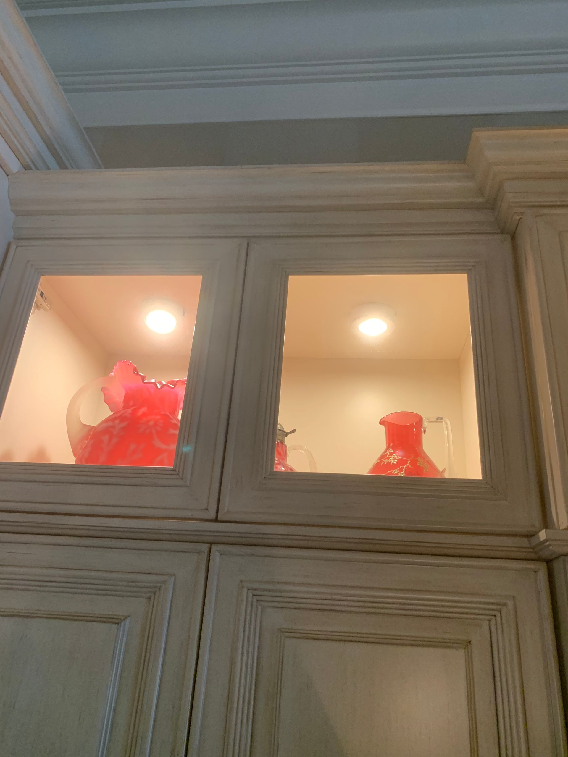 Illuminated cabinet shelves with red decorative vases behind glass panels