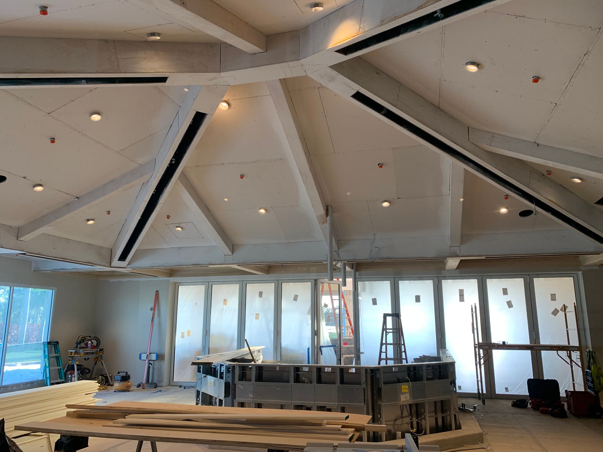 Interior of a room under renovation with exposed ceiling beams, ladders, and construction materials.