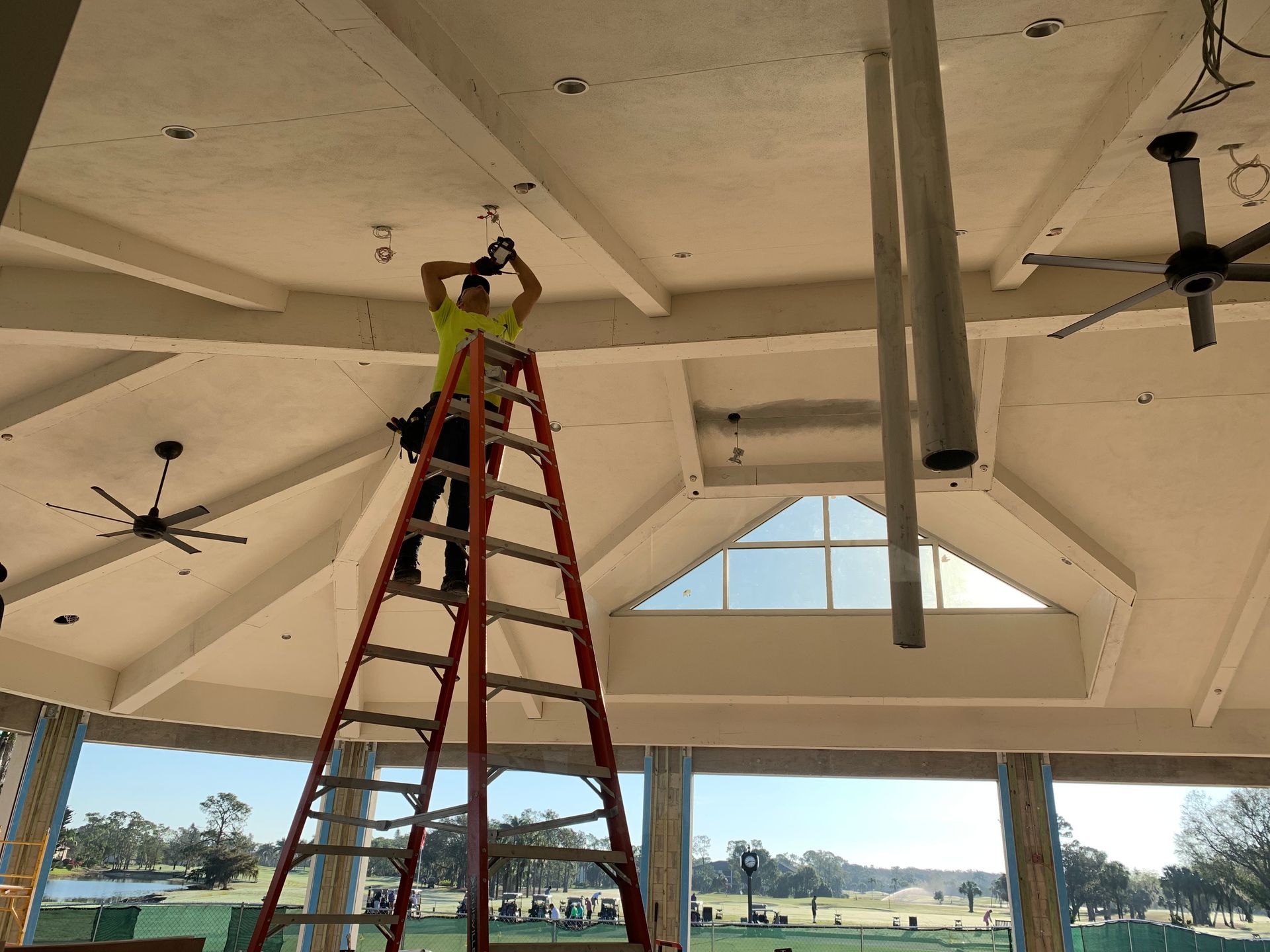 Person on red ladder inspecting white ceiling beams in an open pavilion.