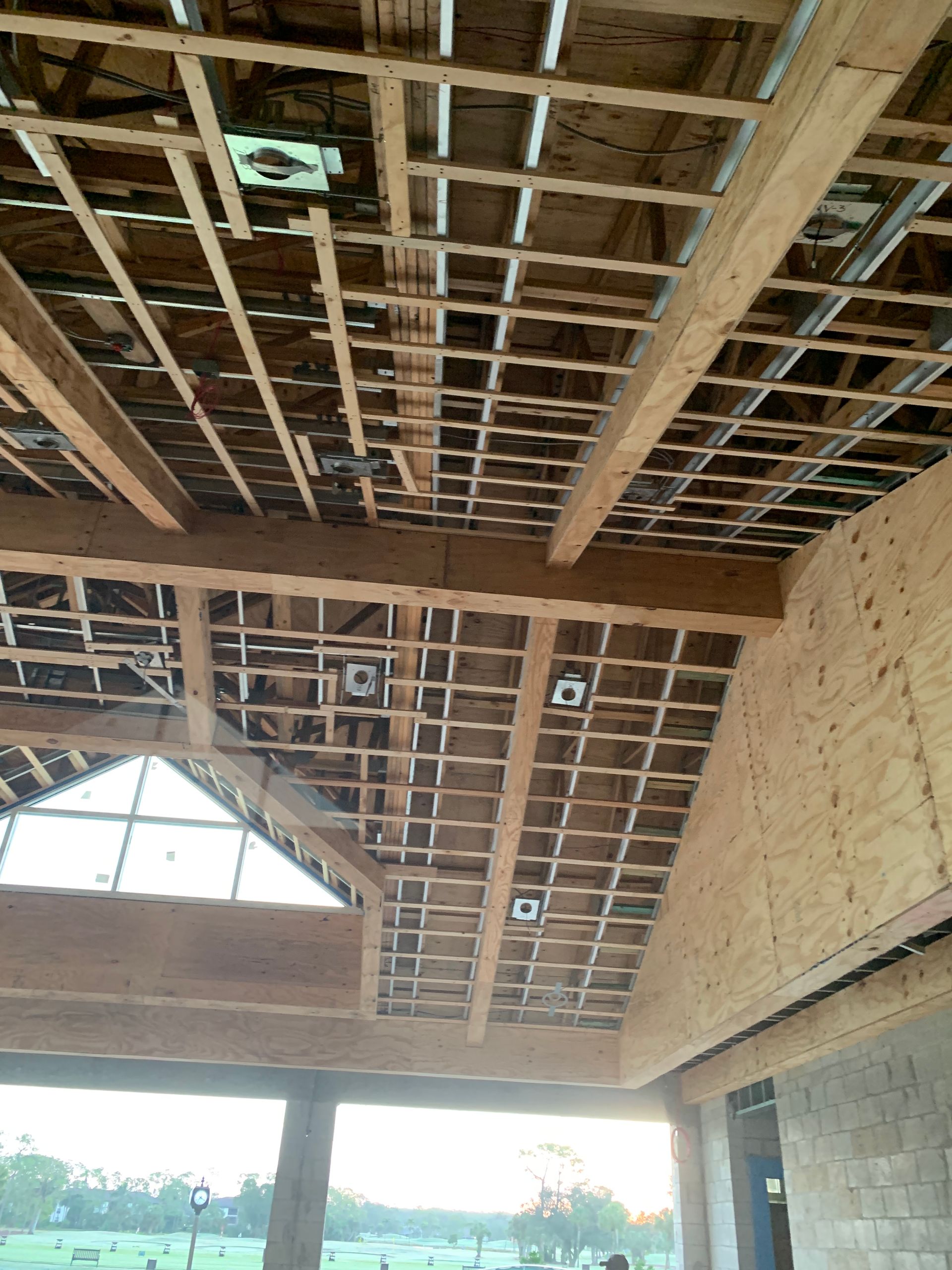 Ceiling under construction with exposed wooden beams and roof framing above a partially open building interior