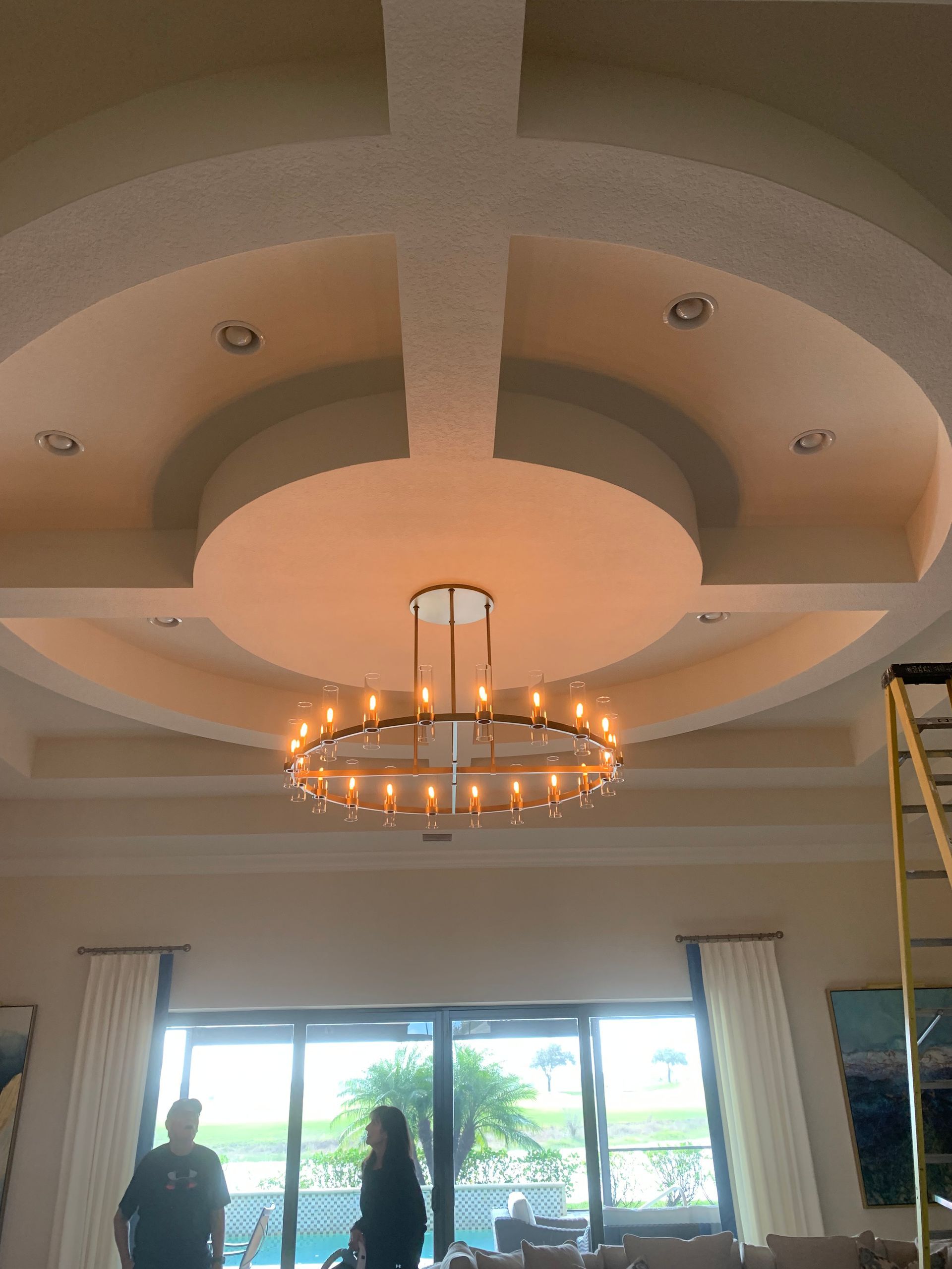 Elegant living room with a large chandelier, tray ceiling, and sliding glass doors to a patio.