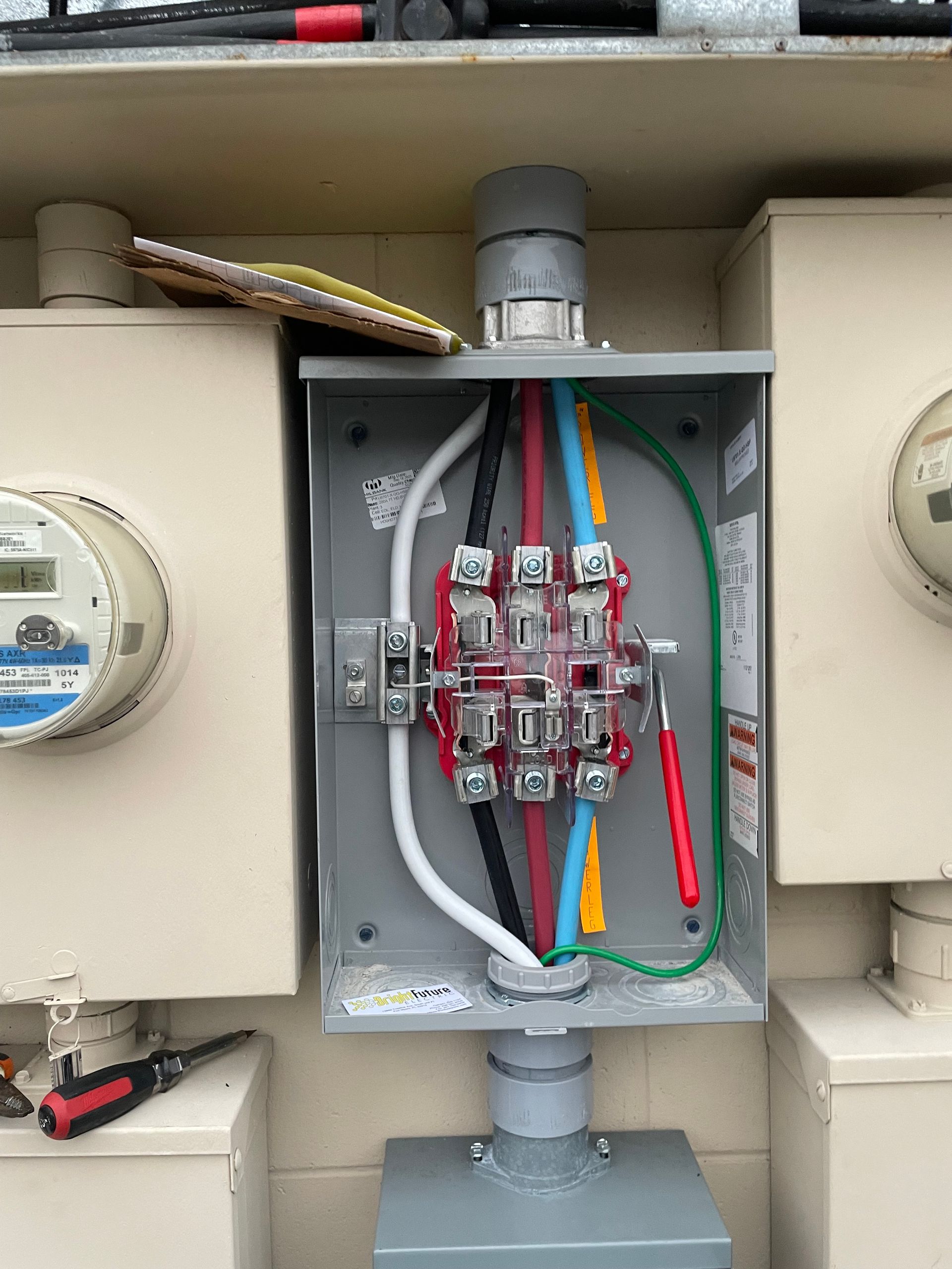 Open electrical meter panel with colored wires and circuit breakers inside a gray utility box