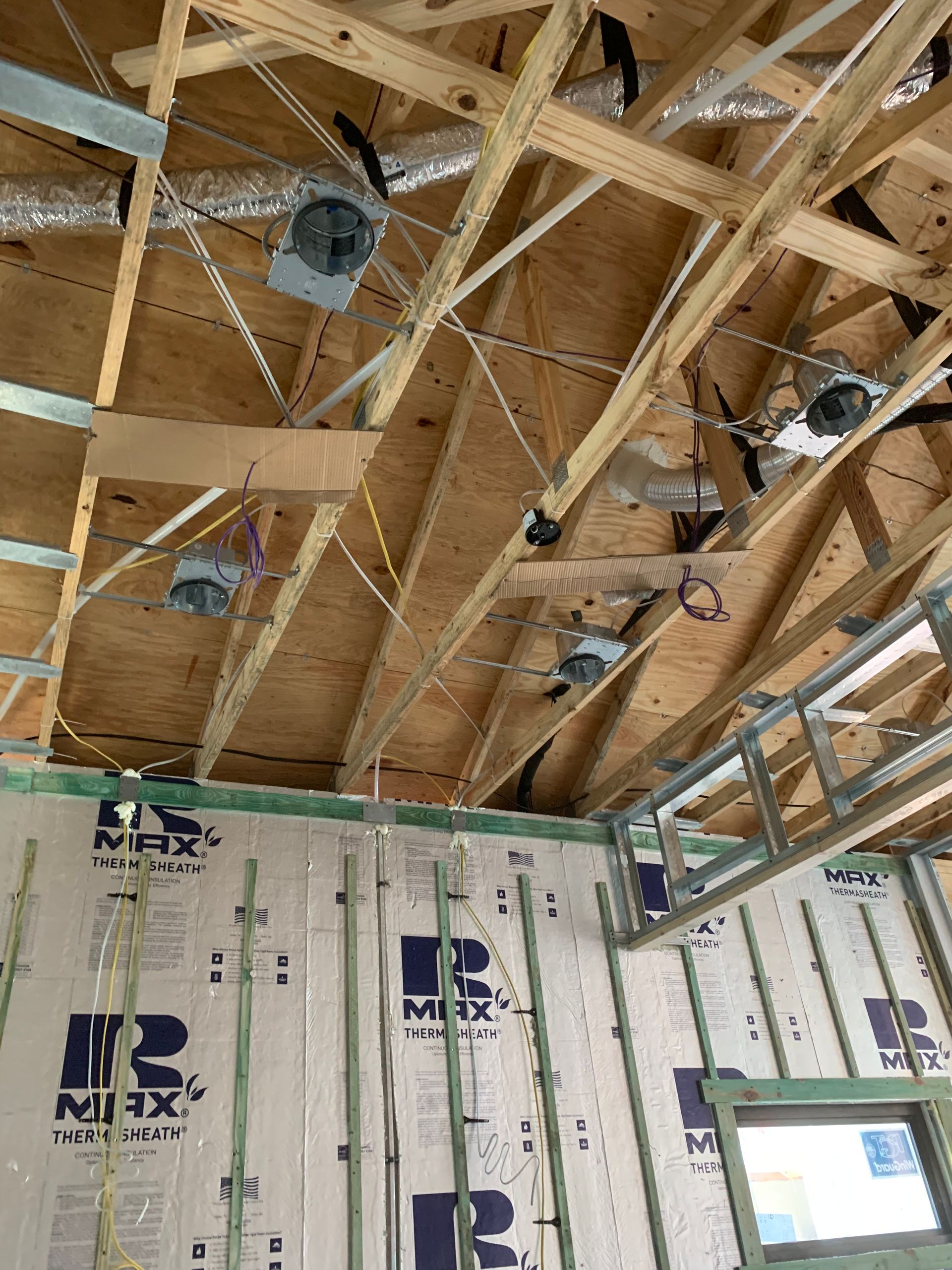 Unfinished room with exposed wooden ceiling trusses, insulation panels, and recessed light fixtures being installed