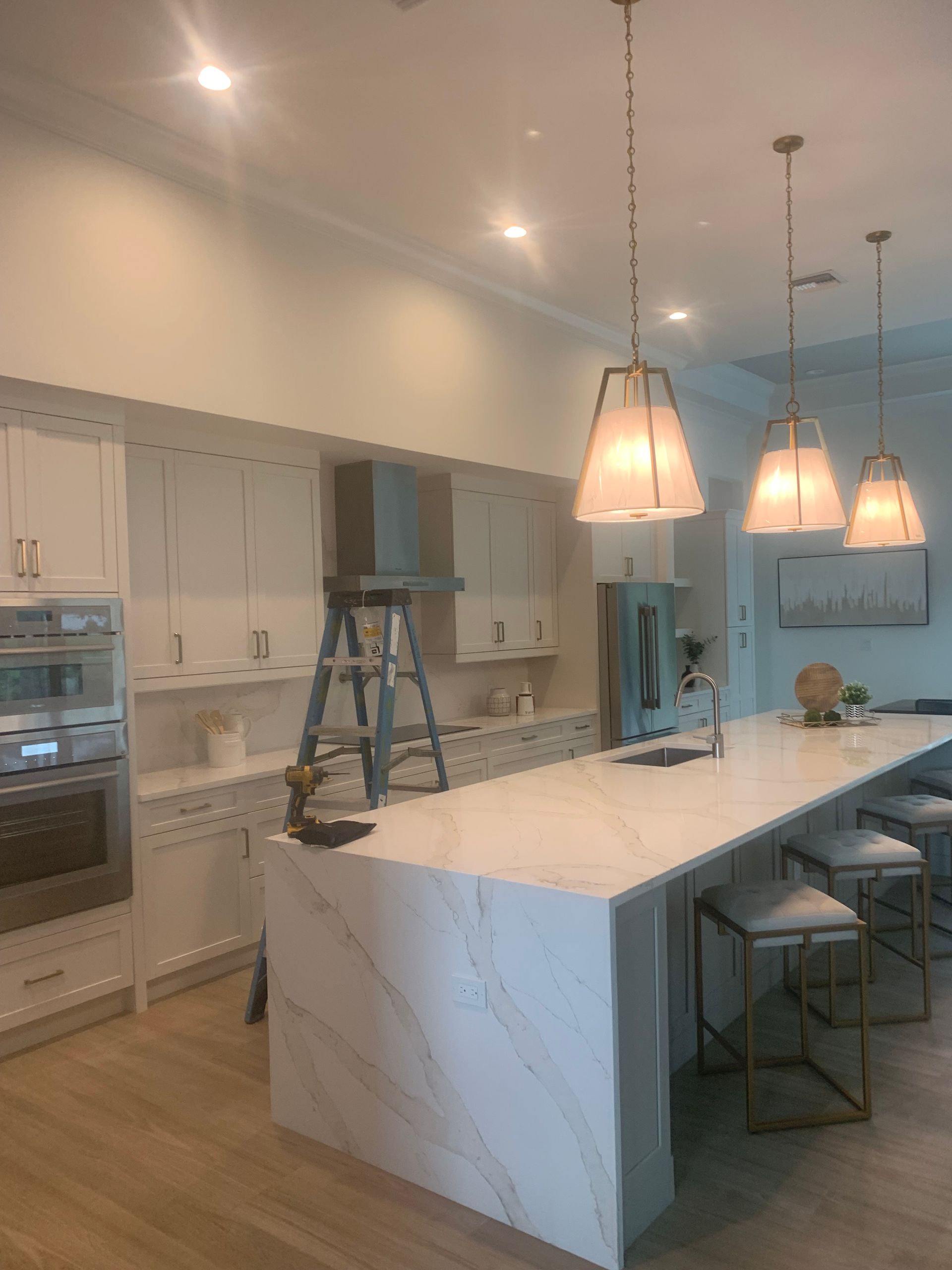 Modern kitchen with white cabinets, marble island, pendant lights, and a step ladder on the counter