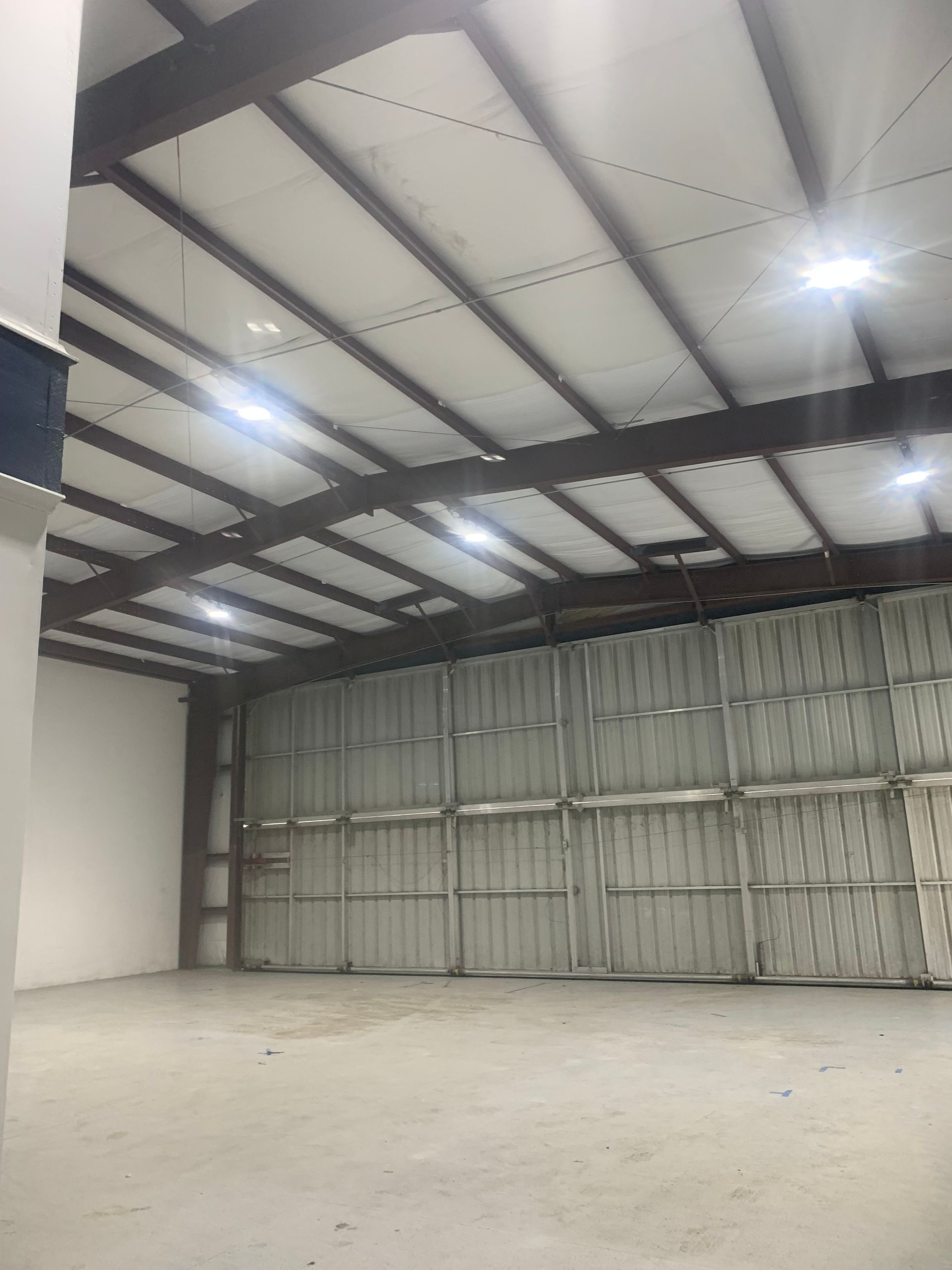 Empty industrial warehouse with a concrete floor, metal walls, and bright overhead lights.