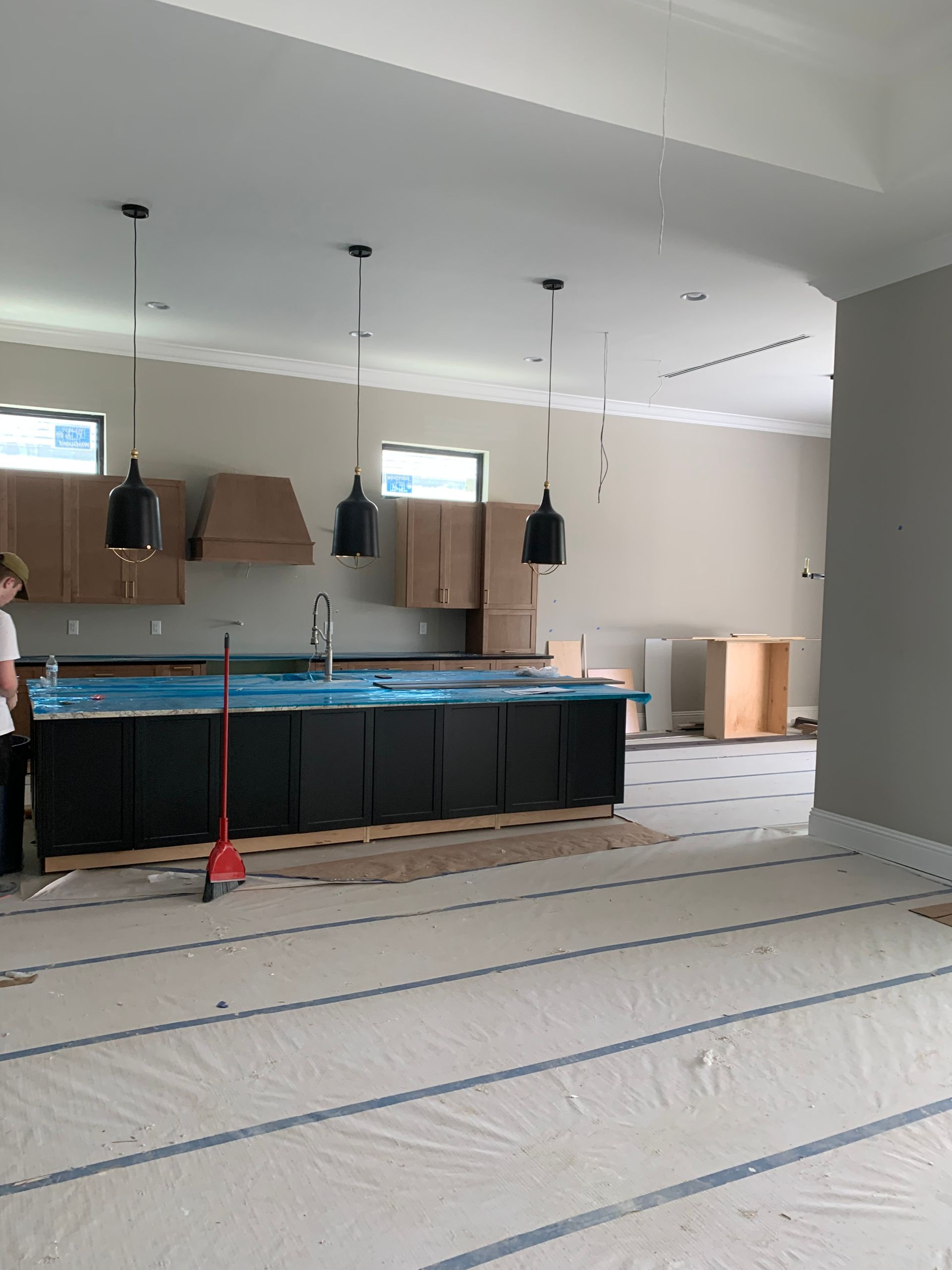 Partially renovated kitchen with black cabinets, hanging pendant lights, and protective floor coverings