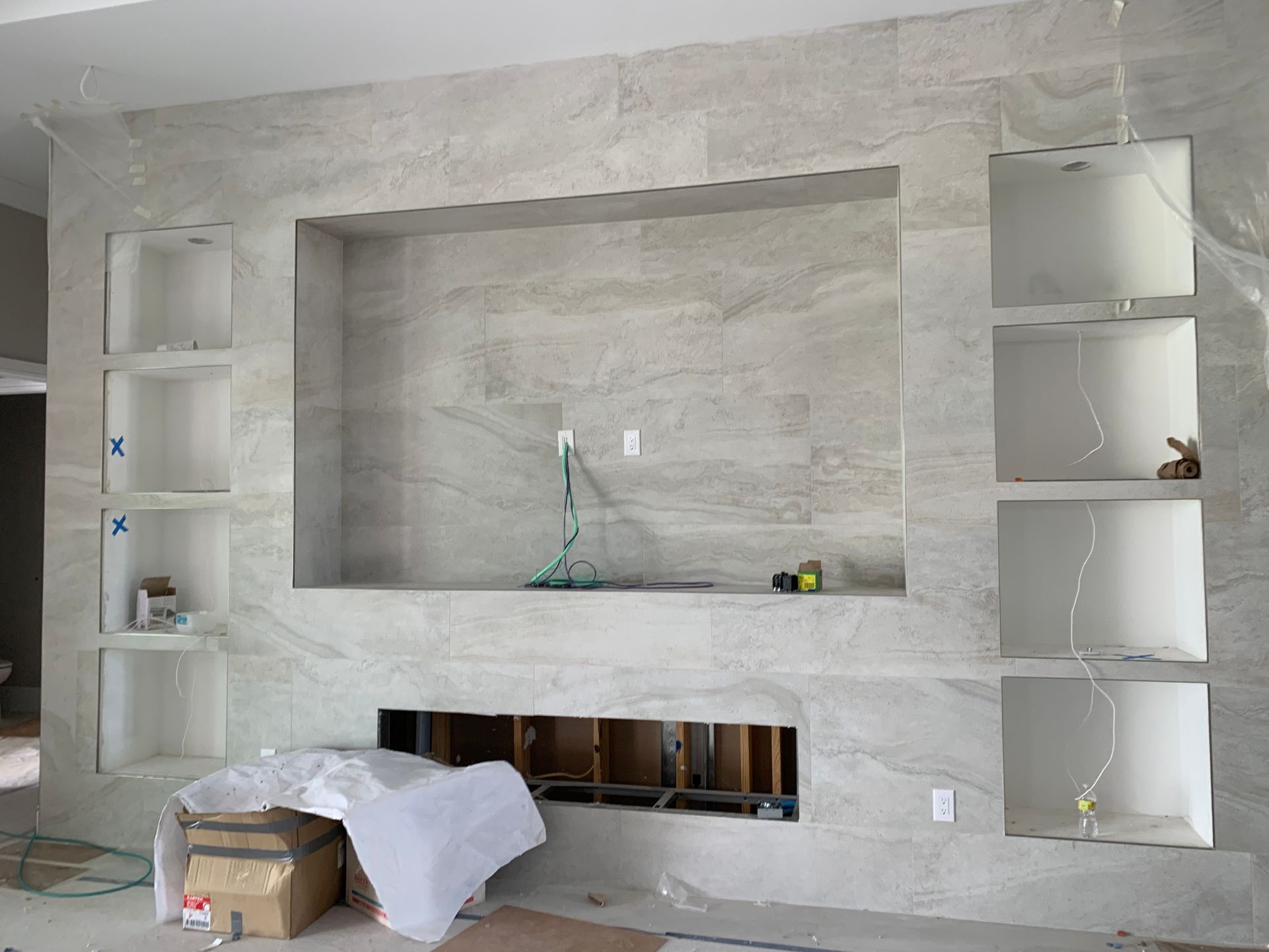 Gray stone fireplace wall with built-in shelves and unfinished wiring in a living room.