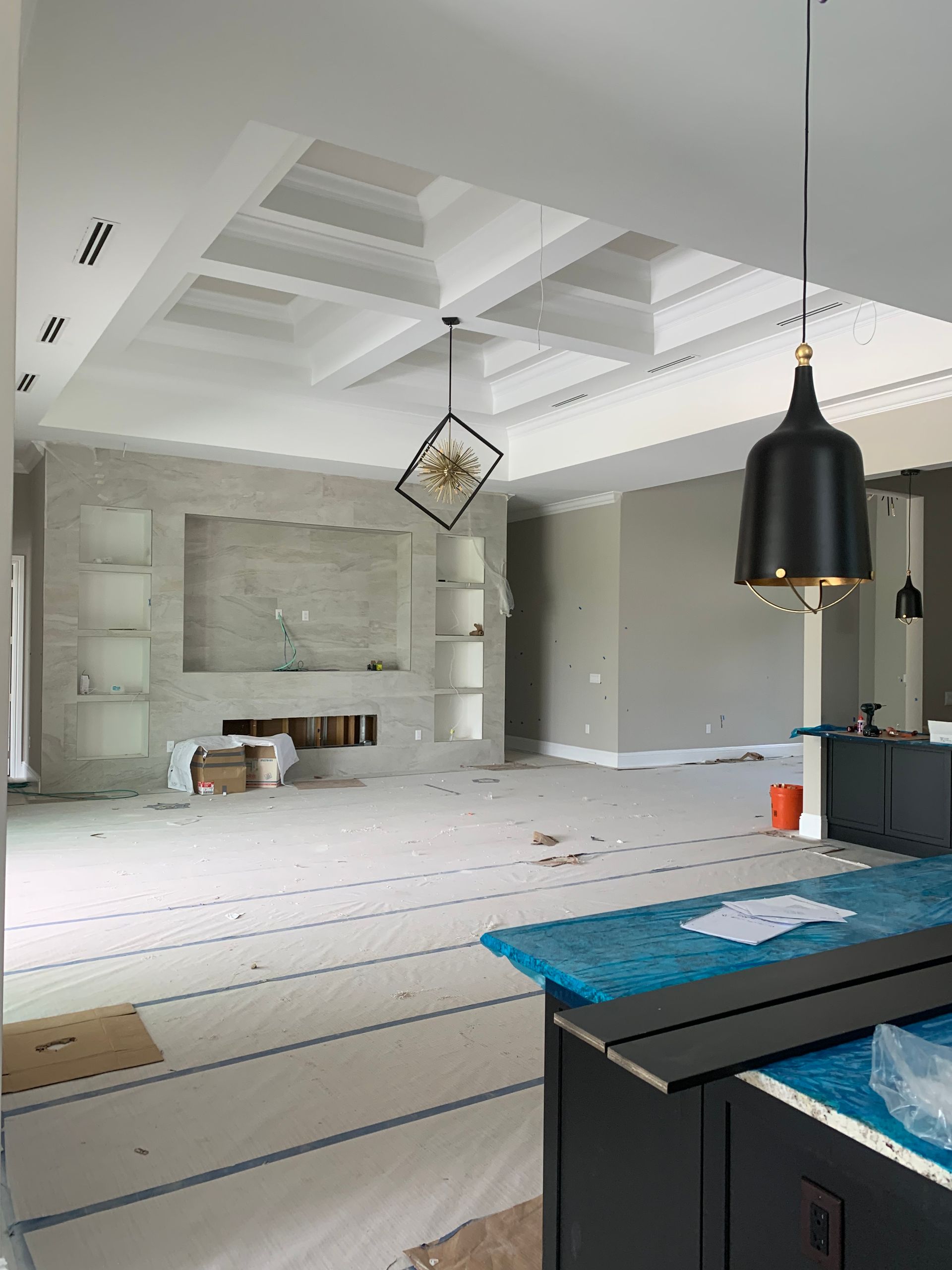 Bright unfinished living room with white ceiling beams, built-in shelves, and a black pendant light on the right.