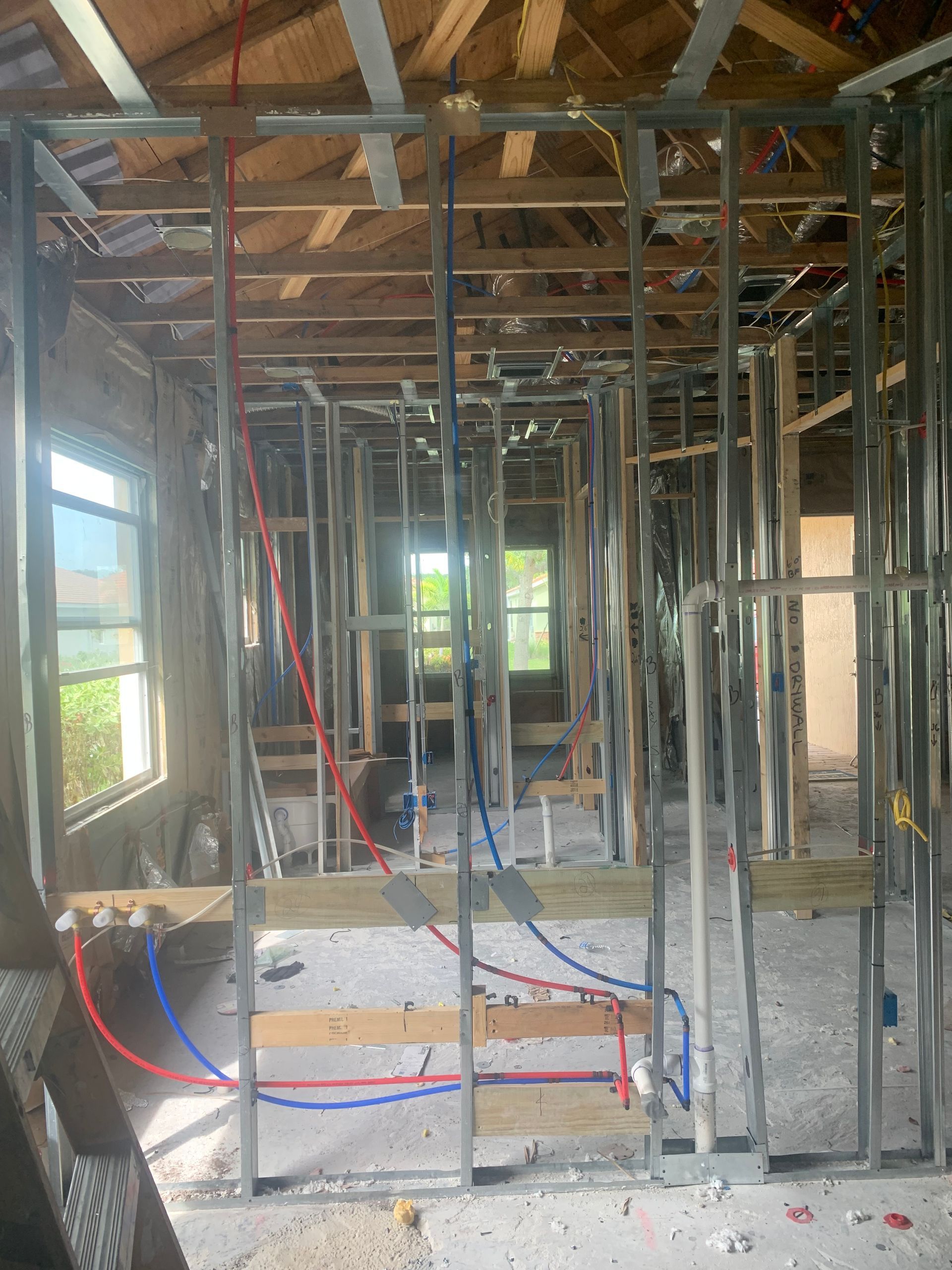 Interior of a house under construction with exposed framing, wiring, and sunlight through windows.