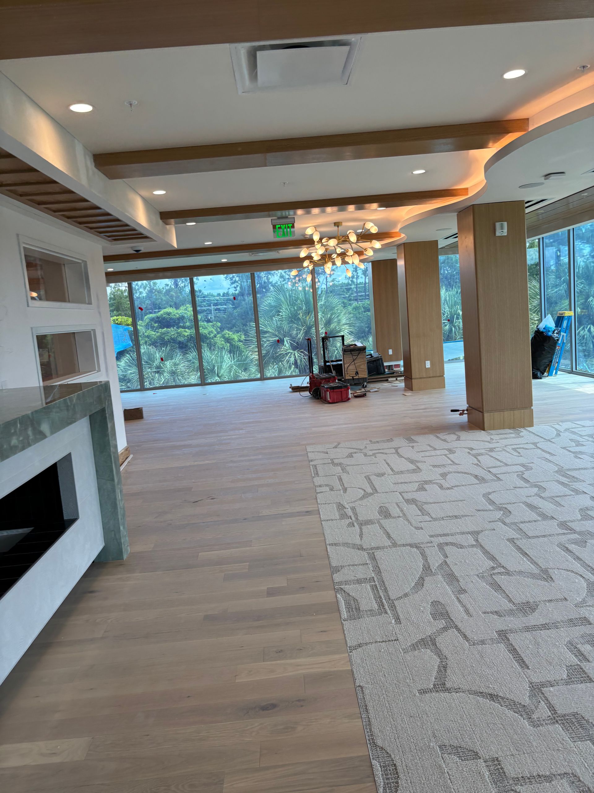 Modern living room with fireplace, wood floors, large windows, and a dining area in the background