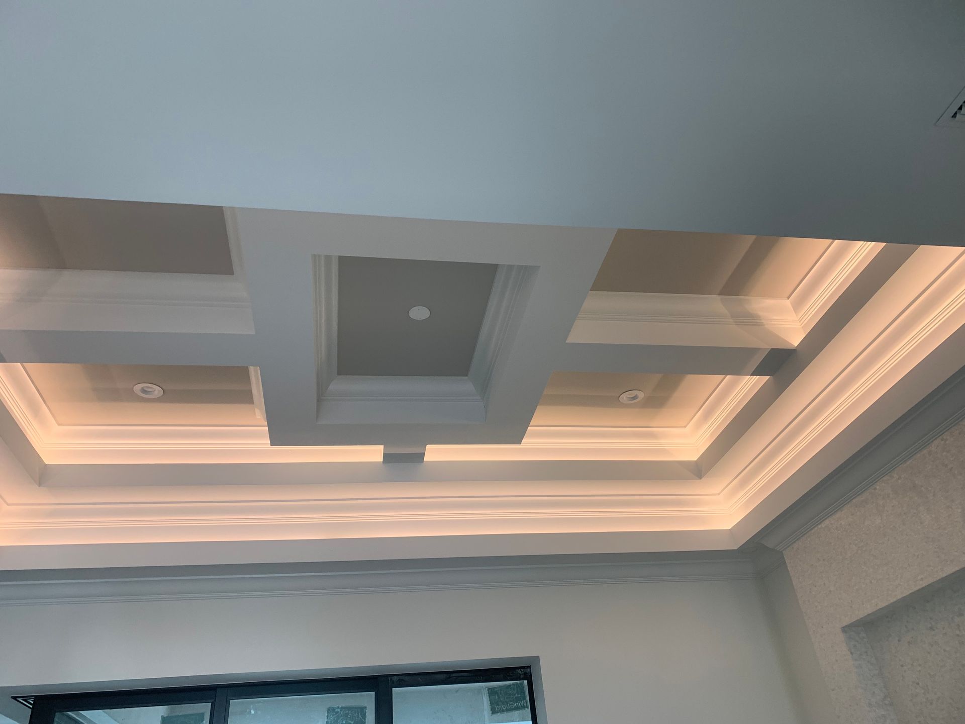 Decorative tray ceiling with recessed lighting and warm cove lights in a modern interior