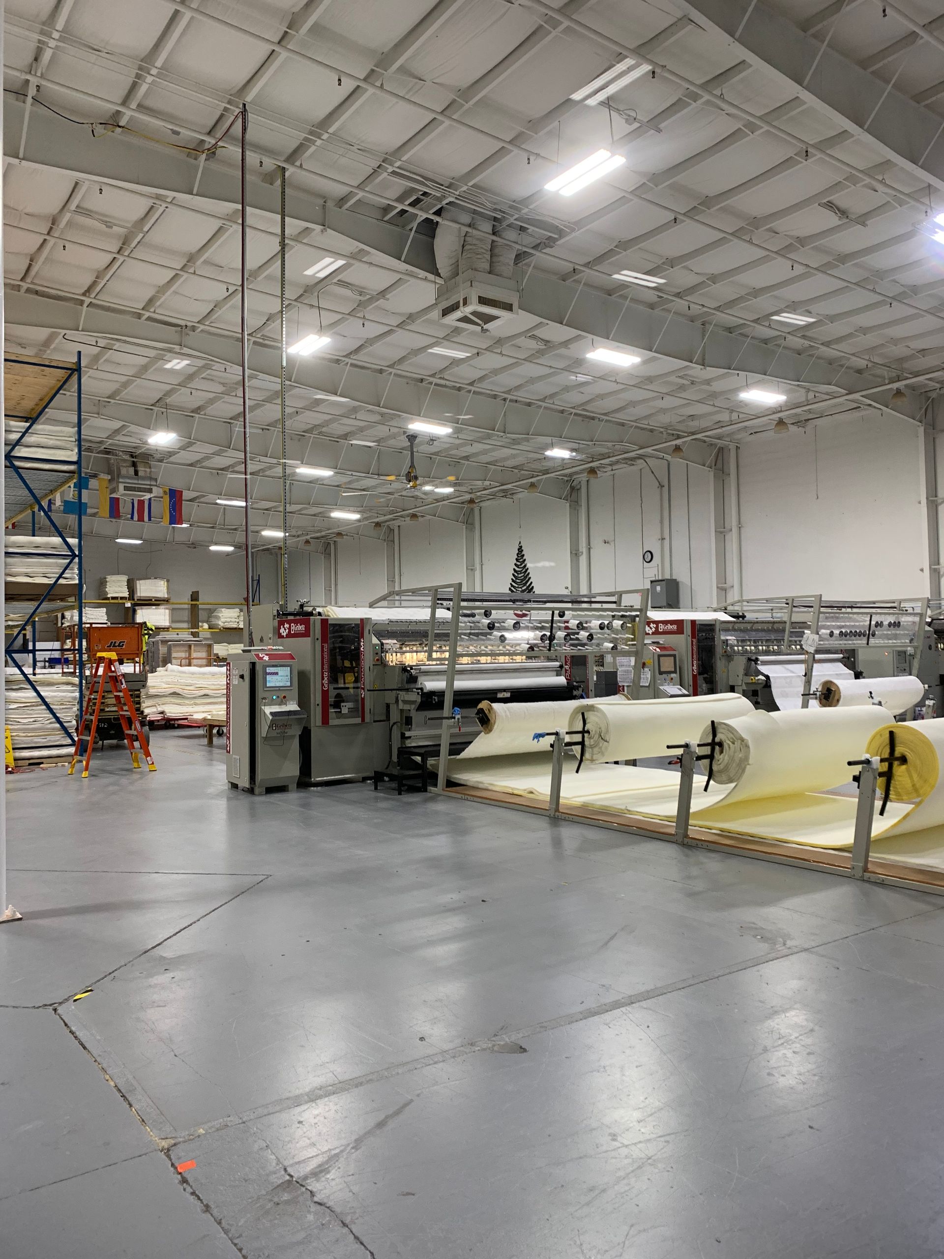 Large industrial workshop with machinery, rolls of material, and bright overhead lights on a polished concrete floor