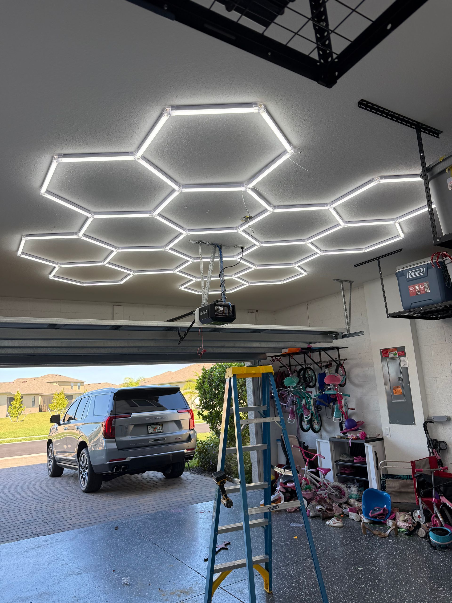 Garage interior with hexagonal LED ceiling lights, a ladder, and an SUV parked near the open door.