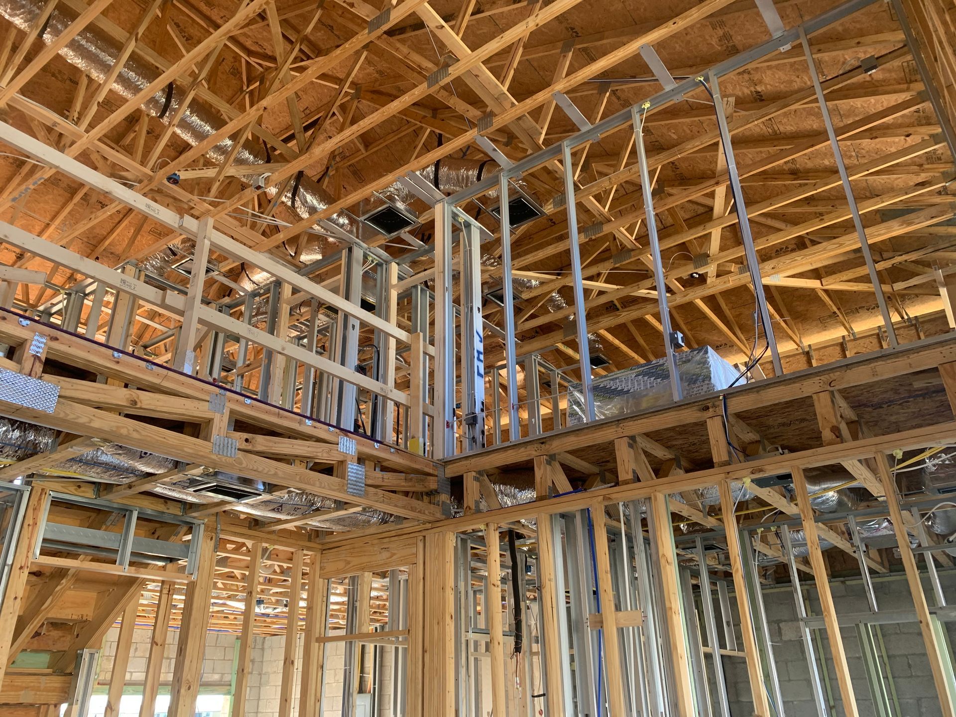 Wood-framed house interior under construction with exposed rafters, studs, and roof trusses