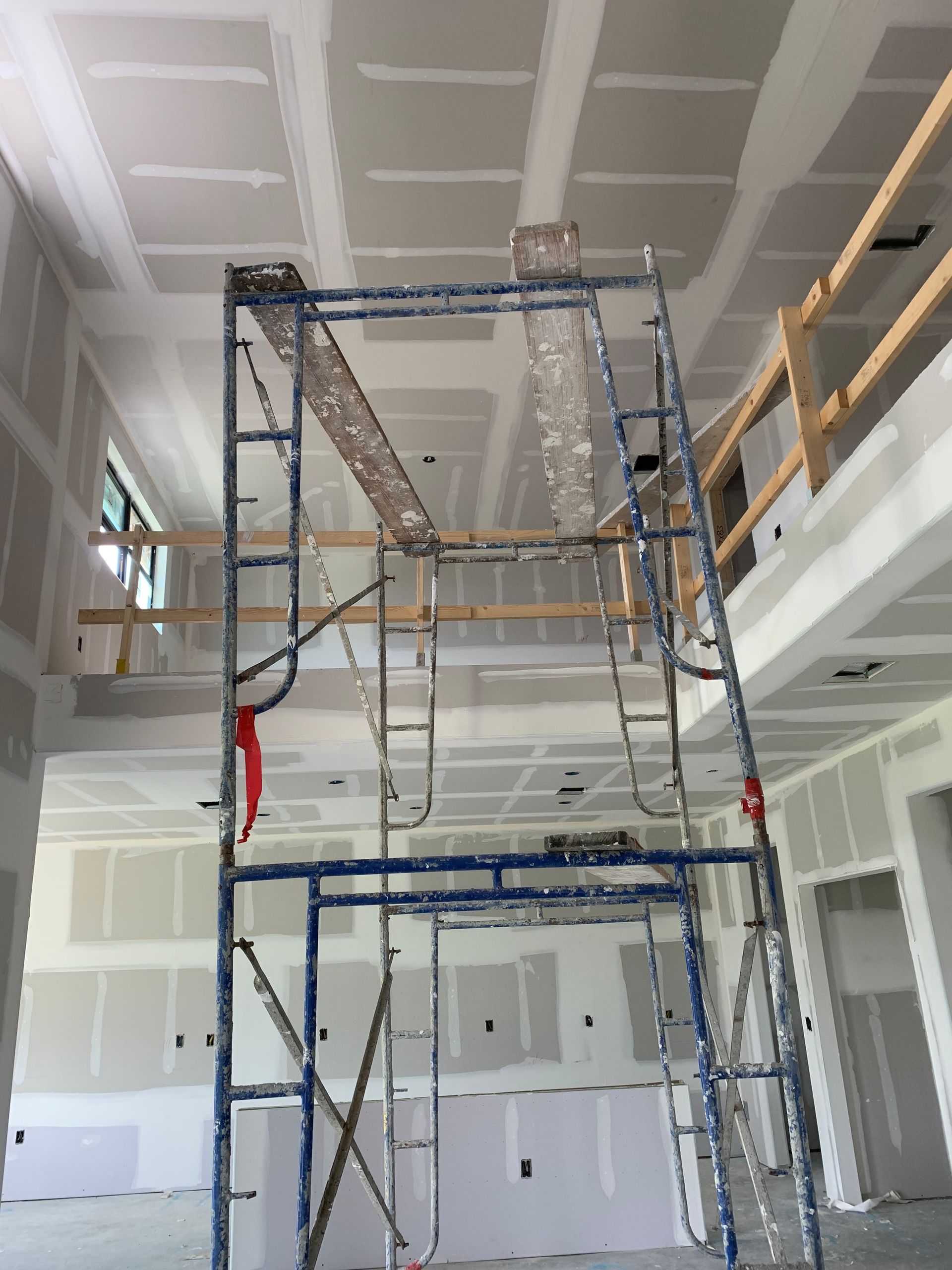Scaffolding in a white interior under construction, with unfinished walls and exposed ceiling beams.