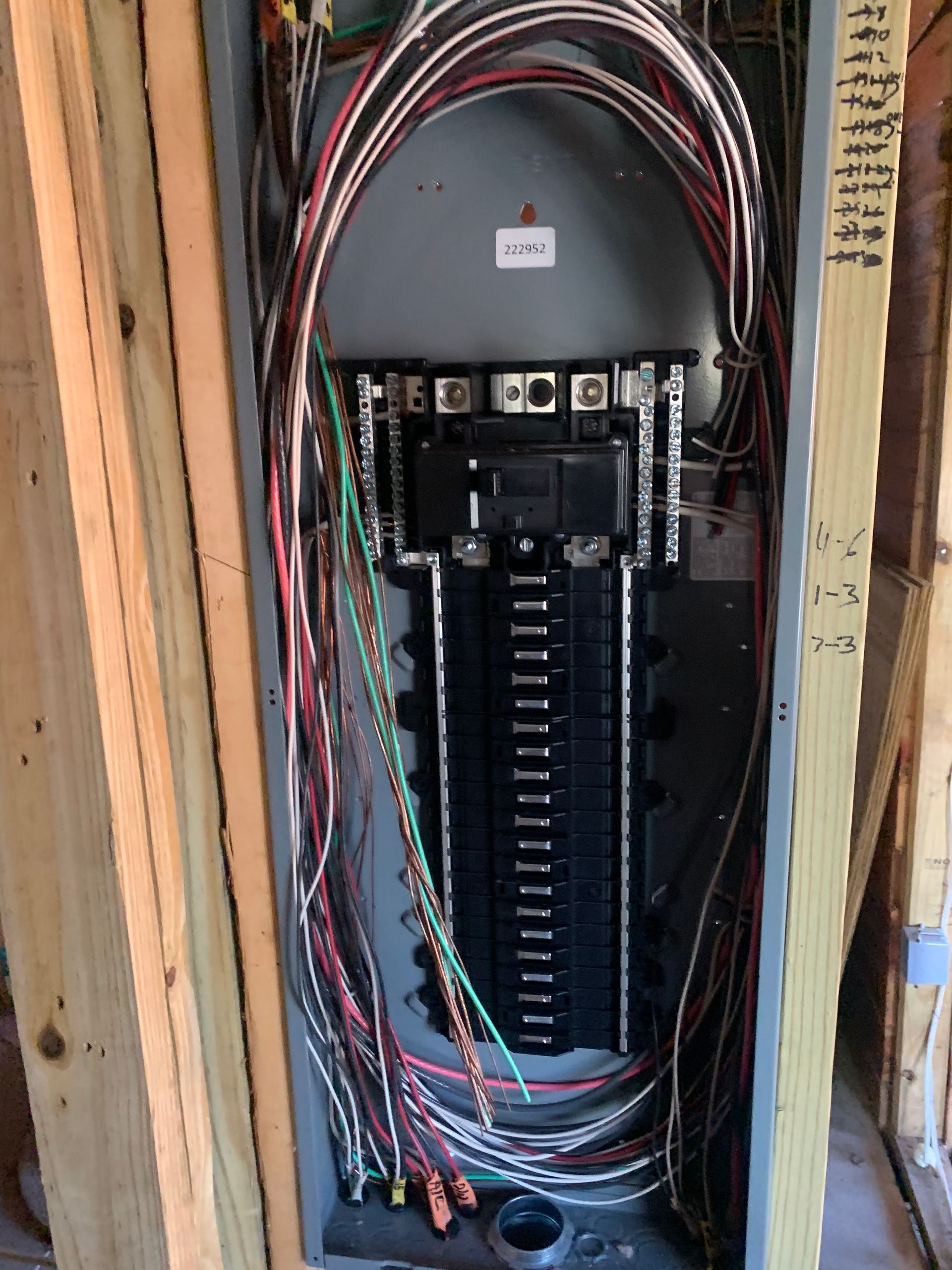 Open electrical breaker panel with exposed multicolored wires in a wall cavity.