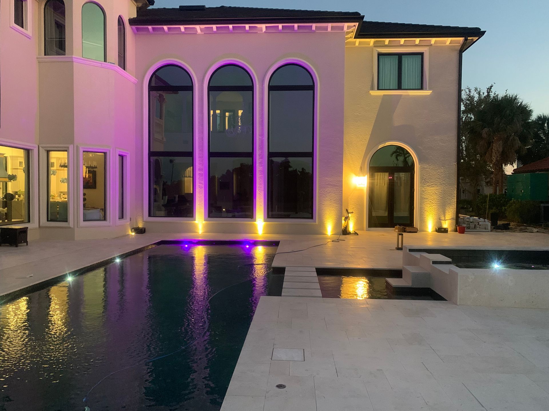 Modern two-story villa with arched windows, lit pool, and purple accent lighting at dusk