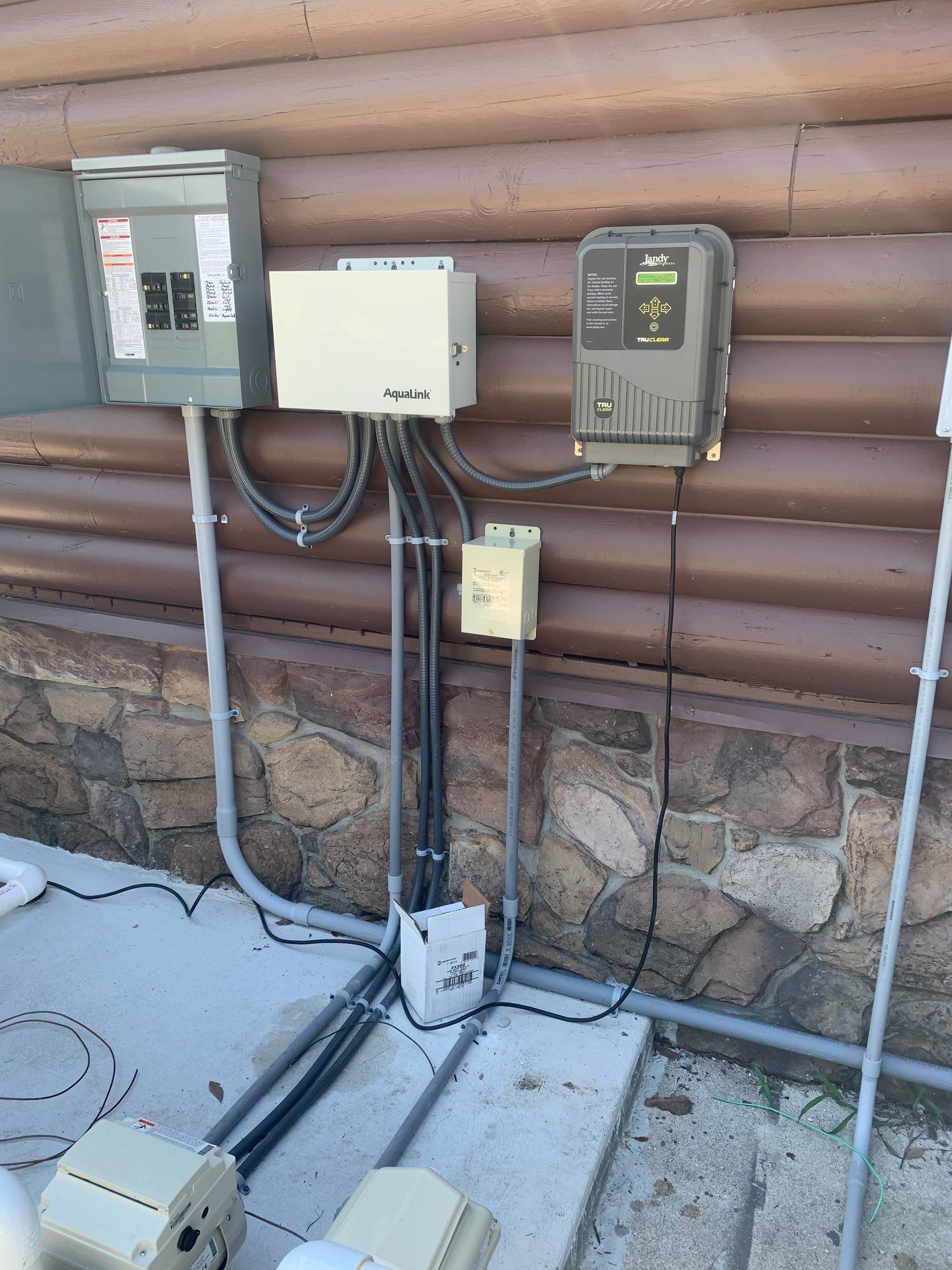 Outdoor utility meters and electrical boxes mounted on a log cabin wall above a snowy ground area