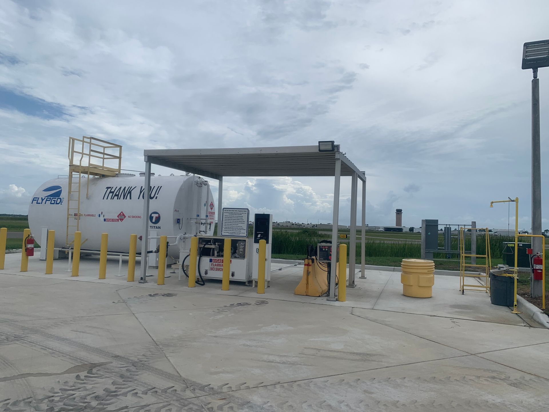 Fueling station with a white tanker truck under a gray canopy in an industrial lot.